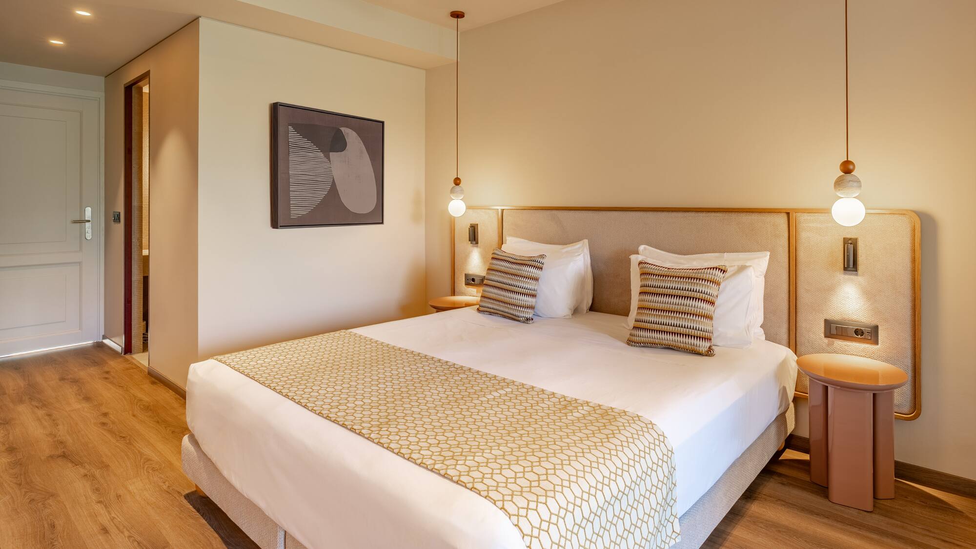 Modern hotel room with large bed, patterned runner, wood floor, and pendant lights.
