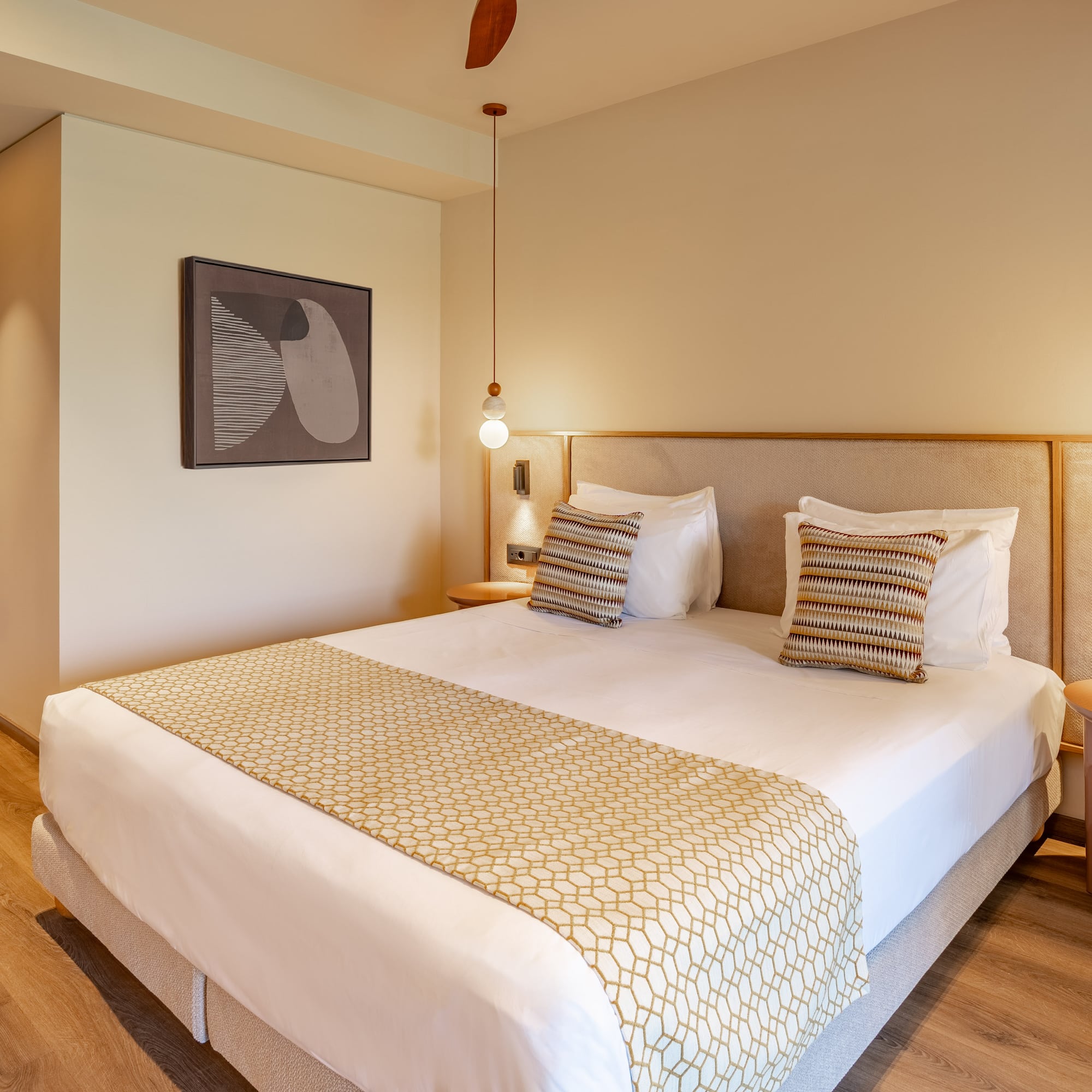 Modern hotel room with large bed, patterned runner, wood floor, and pendant lights.