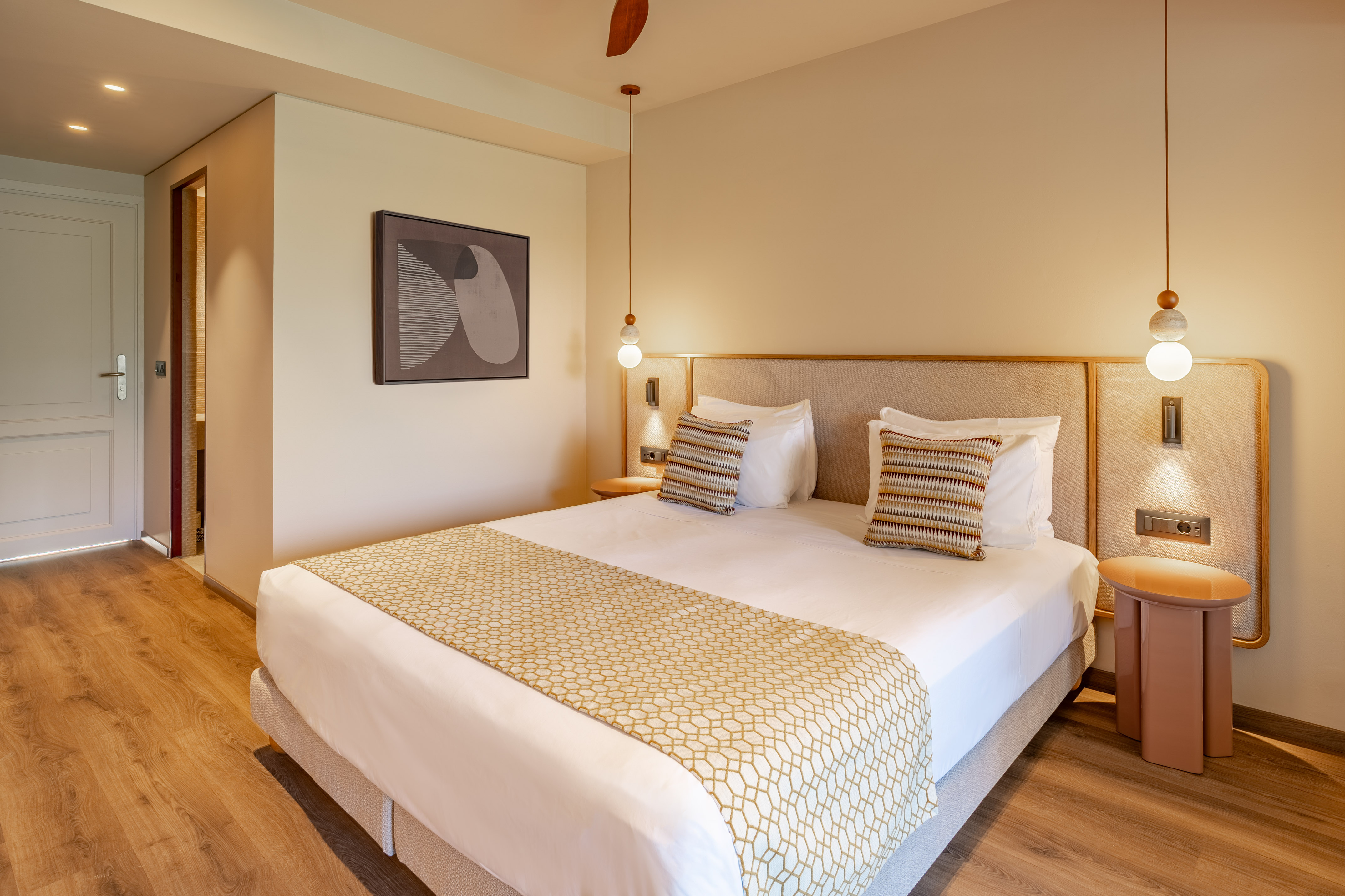 Modern hotel room with large bed, patterned runner, wood floor, and pendant lights.