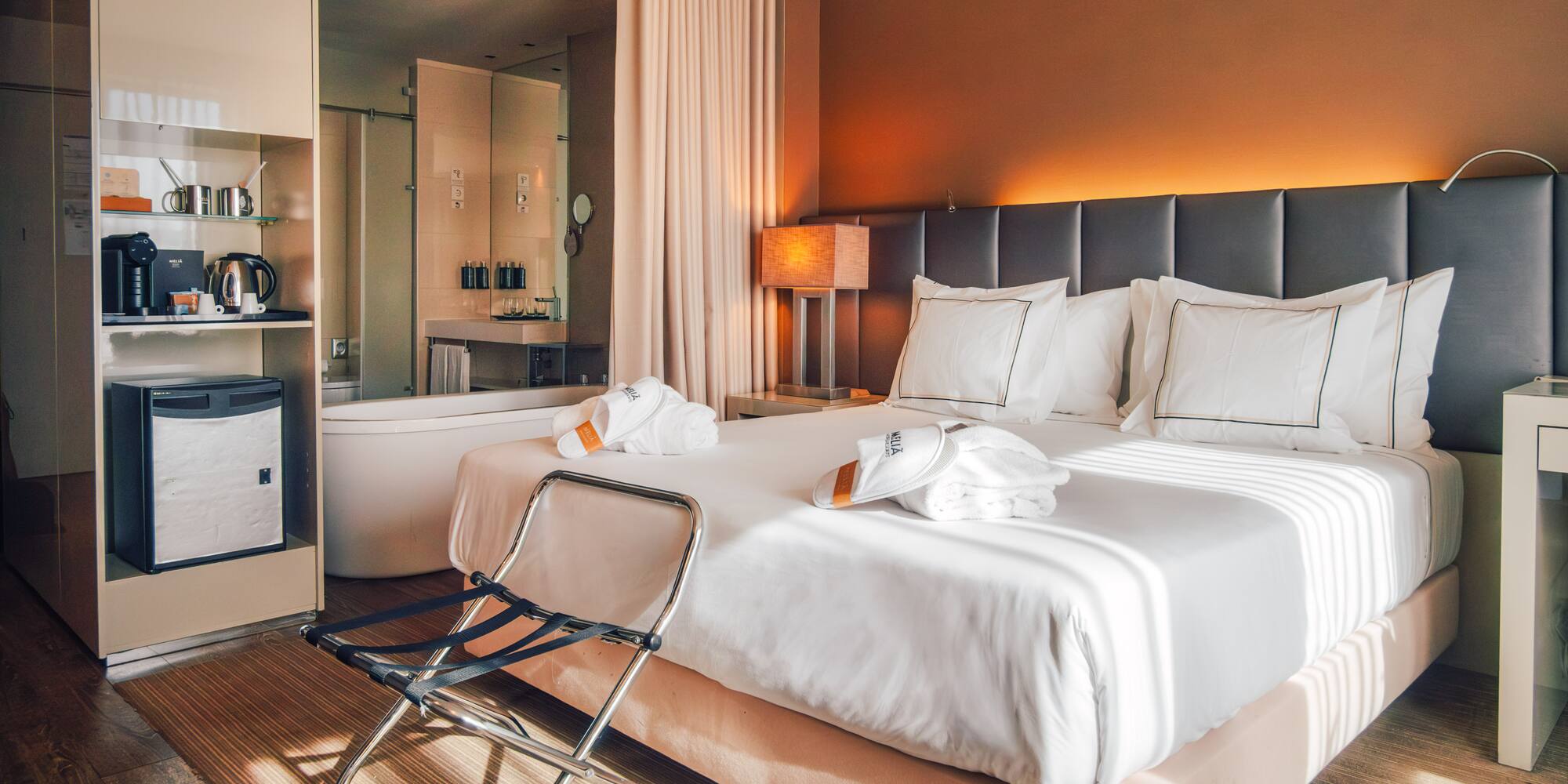 Contemporary hotel room with king bed, open bathroom, and warm ambient lighting.