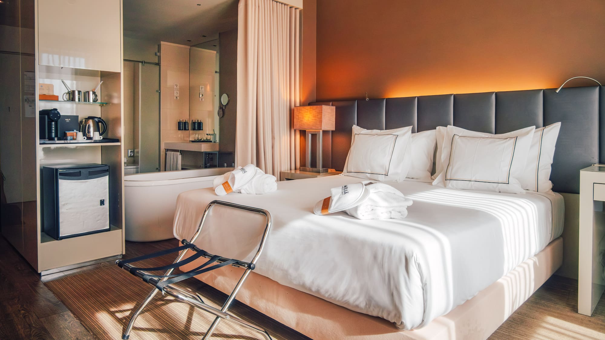 Contemporary hotel room with king bed, open bathroom, and warm ambient lighting.