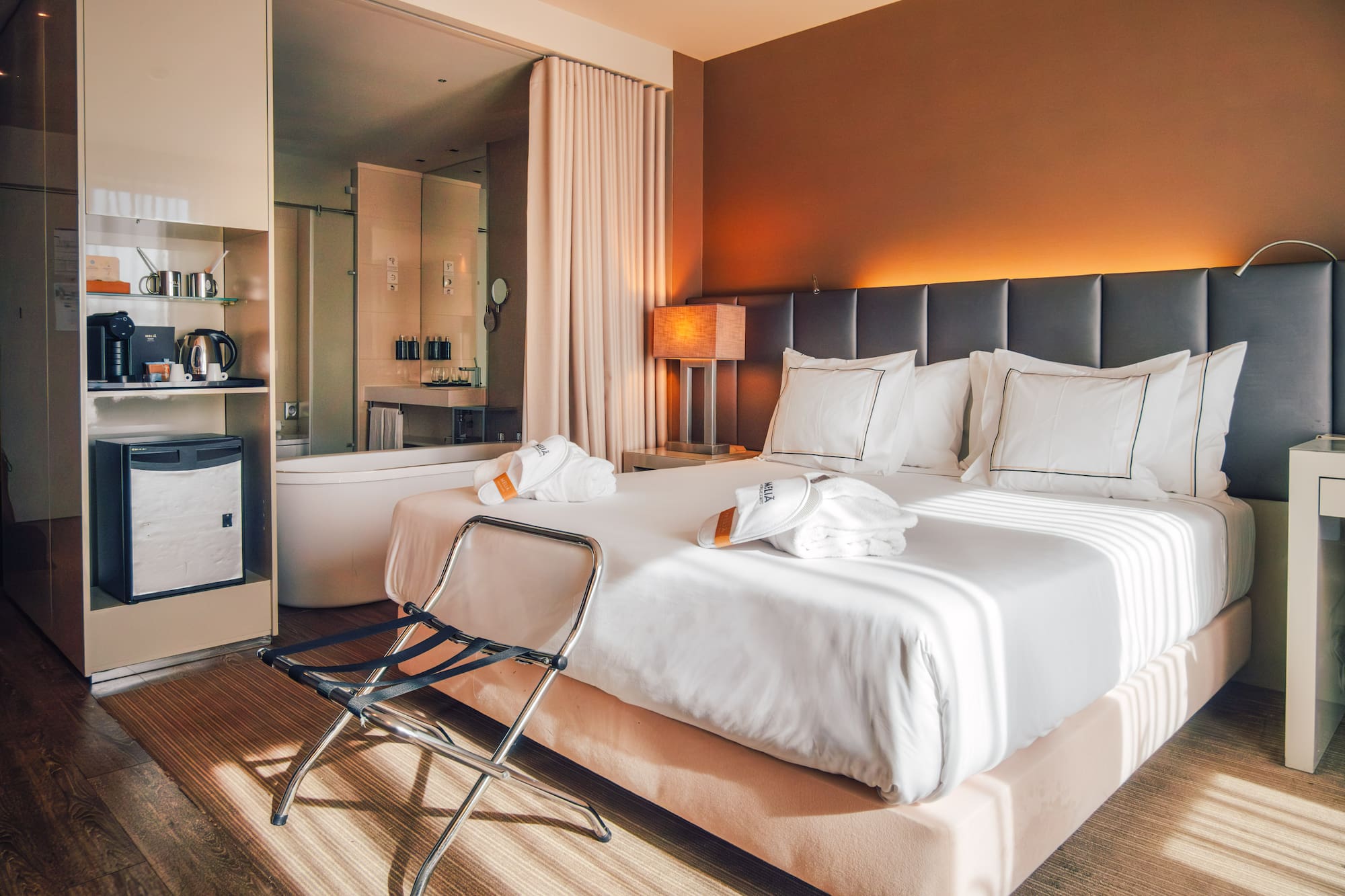 Contemporary hotel room with king bed, open bathroom, and warm ambient lighting.