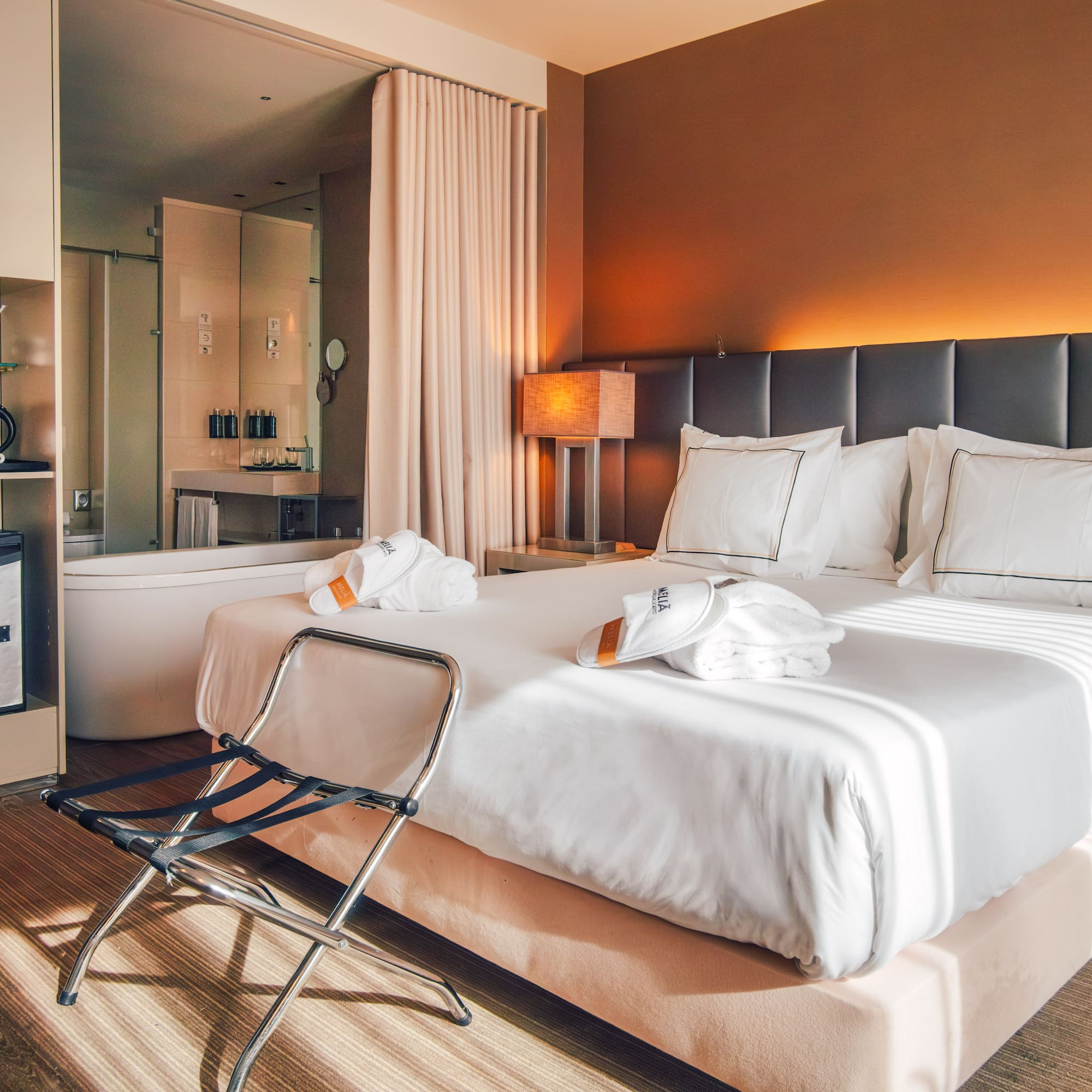 Contemporary hotel room with king bed, open bathroom, and warm ambient lighting.