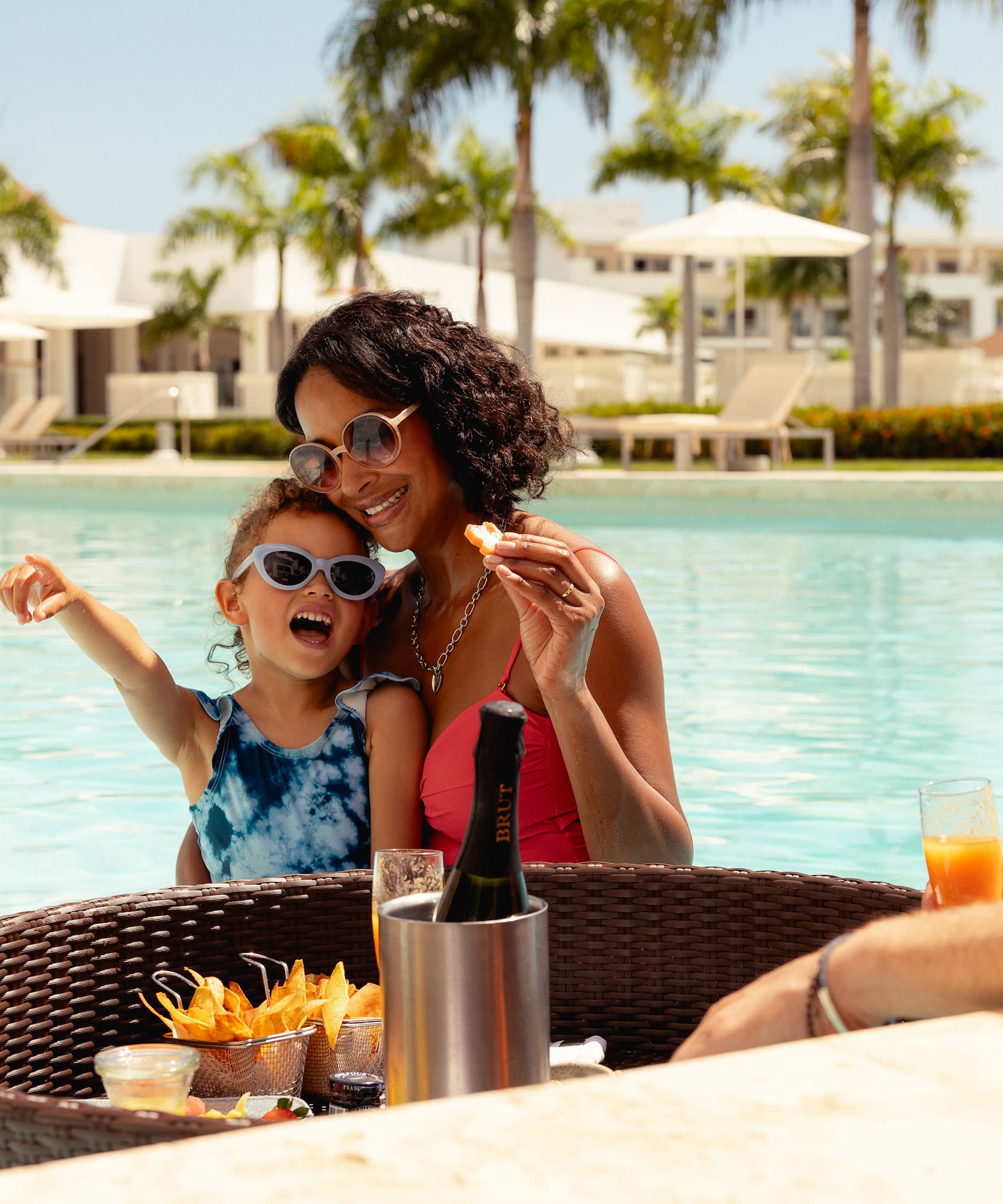 Family vacation at resort pool bar with child, snacks, and champagne.