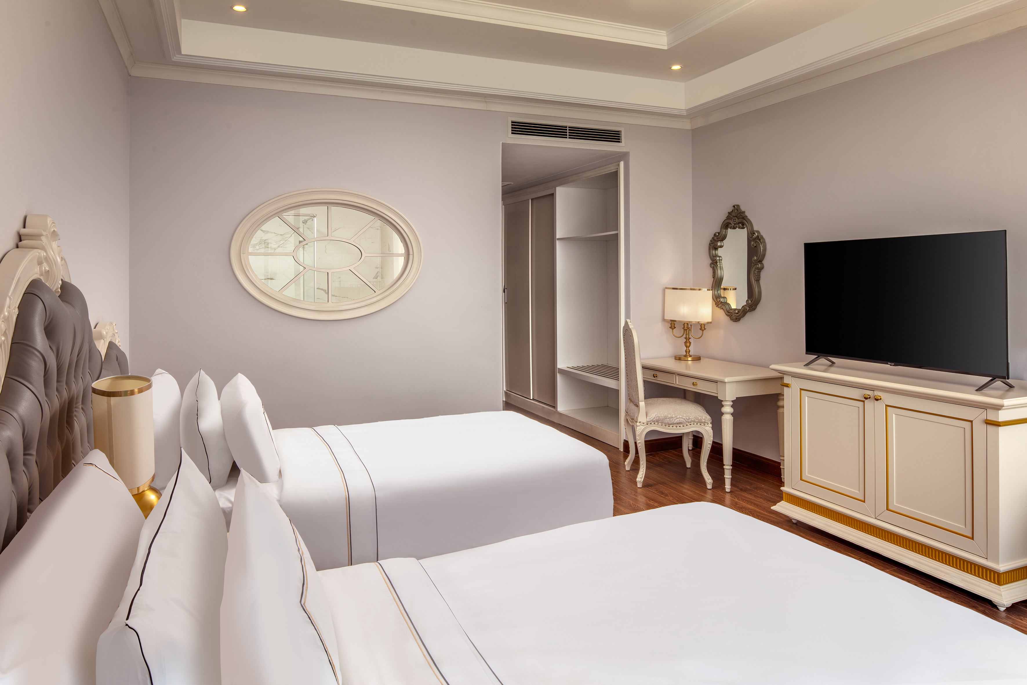 Elegant hotel room with twin beds, TV, vanity, and closet.