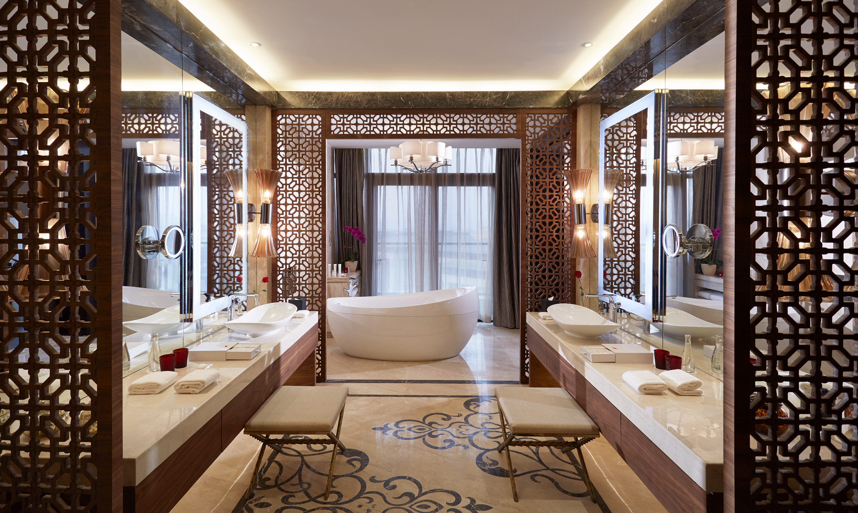 Spacious luxury bathroom with freestanding tub, dual vanities, ornate screens.