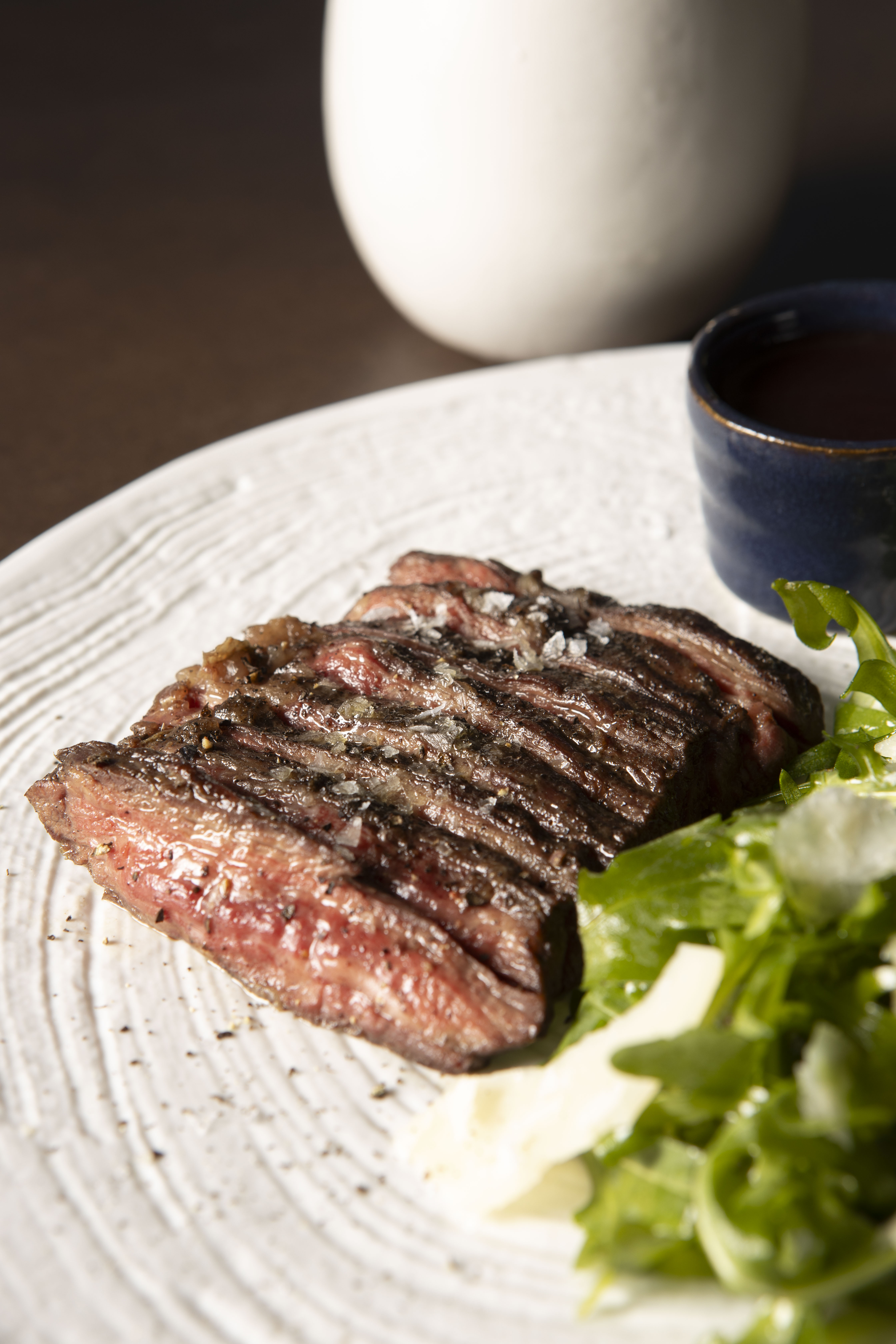 Medium-rare sliced steak with coarse salt, arugula salad, and dipping sauce.