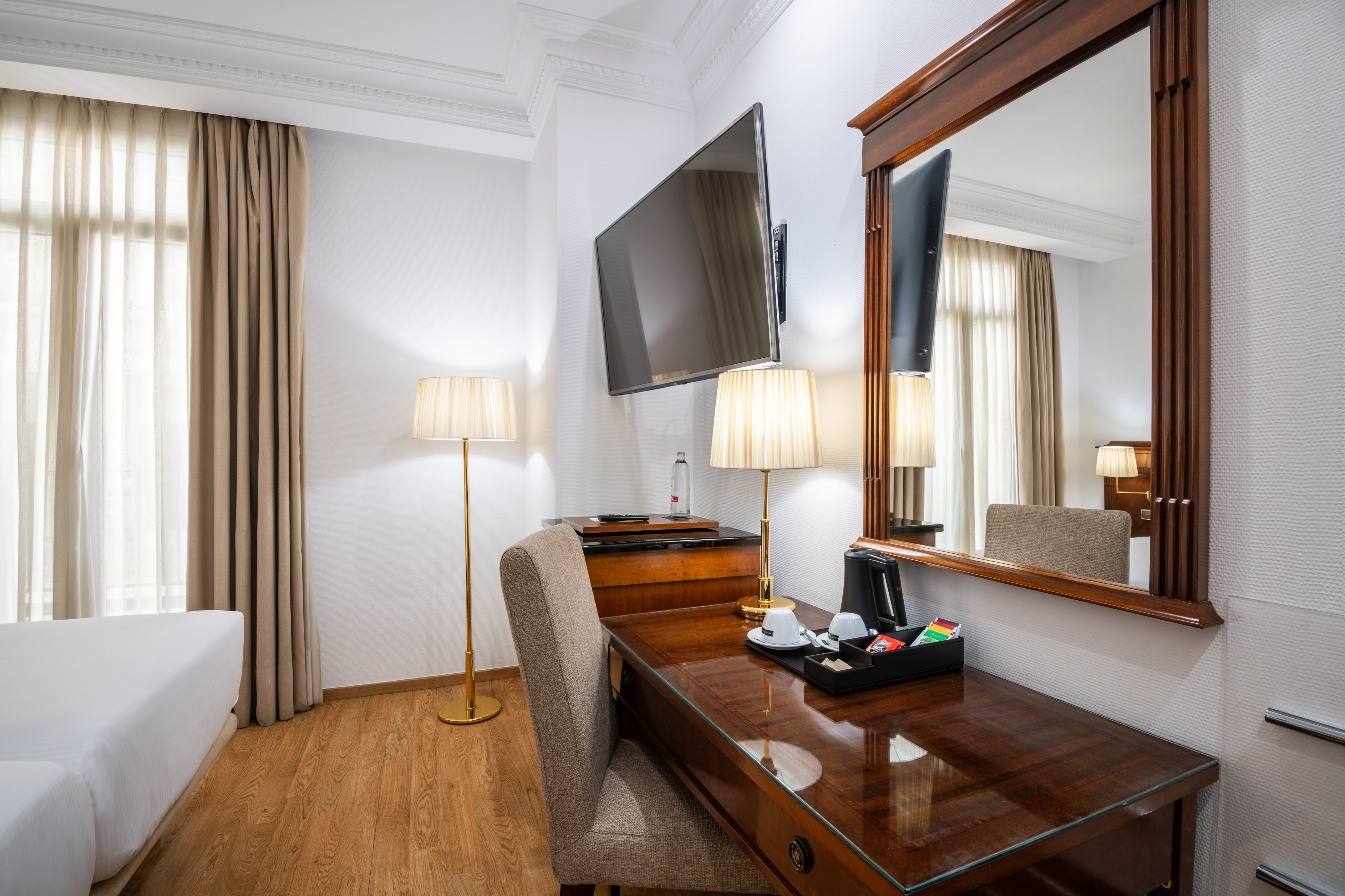 Hotel guest room with desk, TV, amenities, and warm wooden floor.