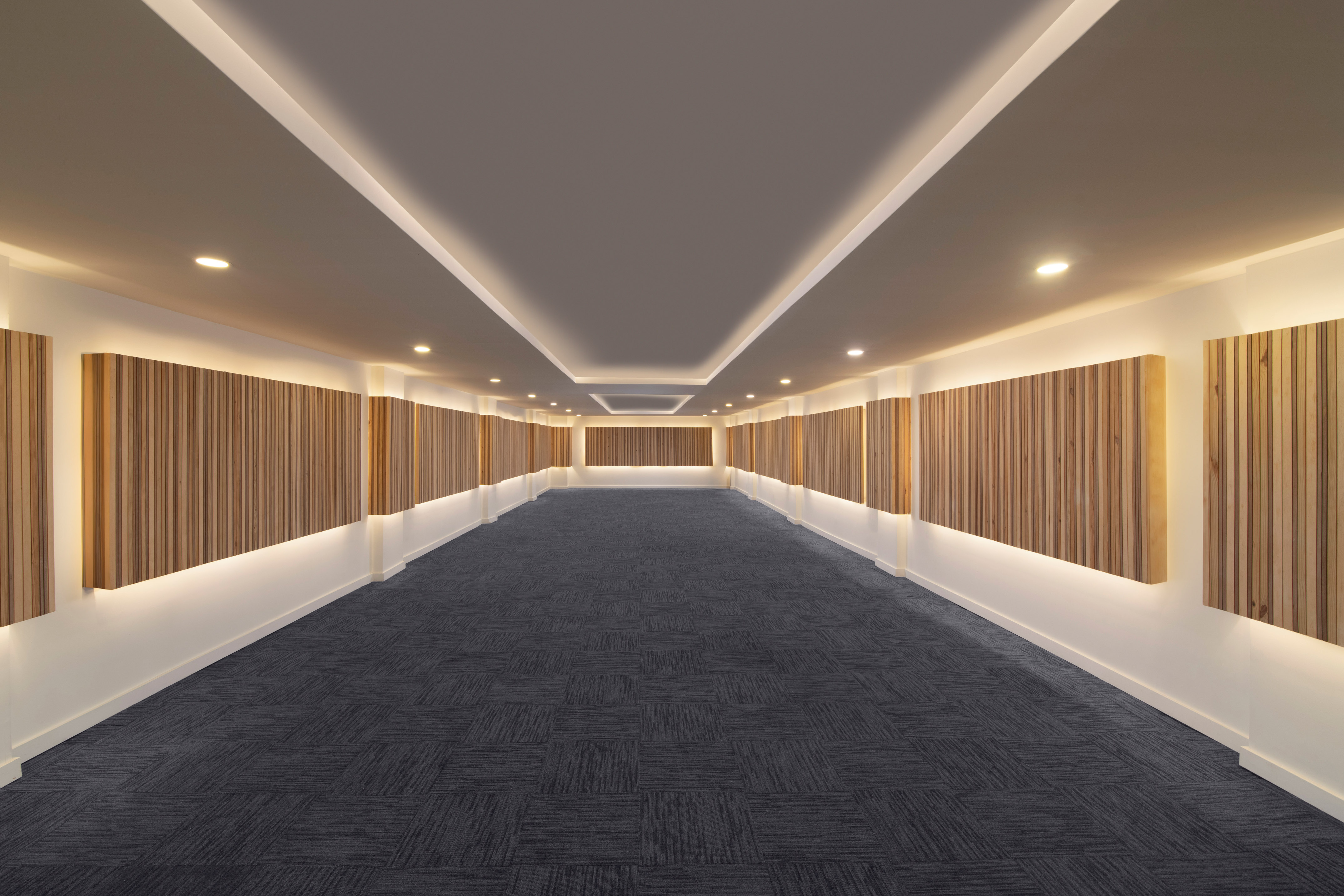 Long modern hallway with wood wall panels, cove lighting, and patterned carpet.