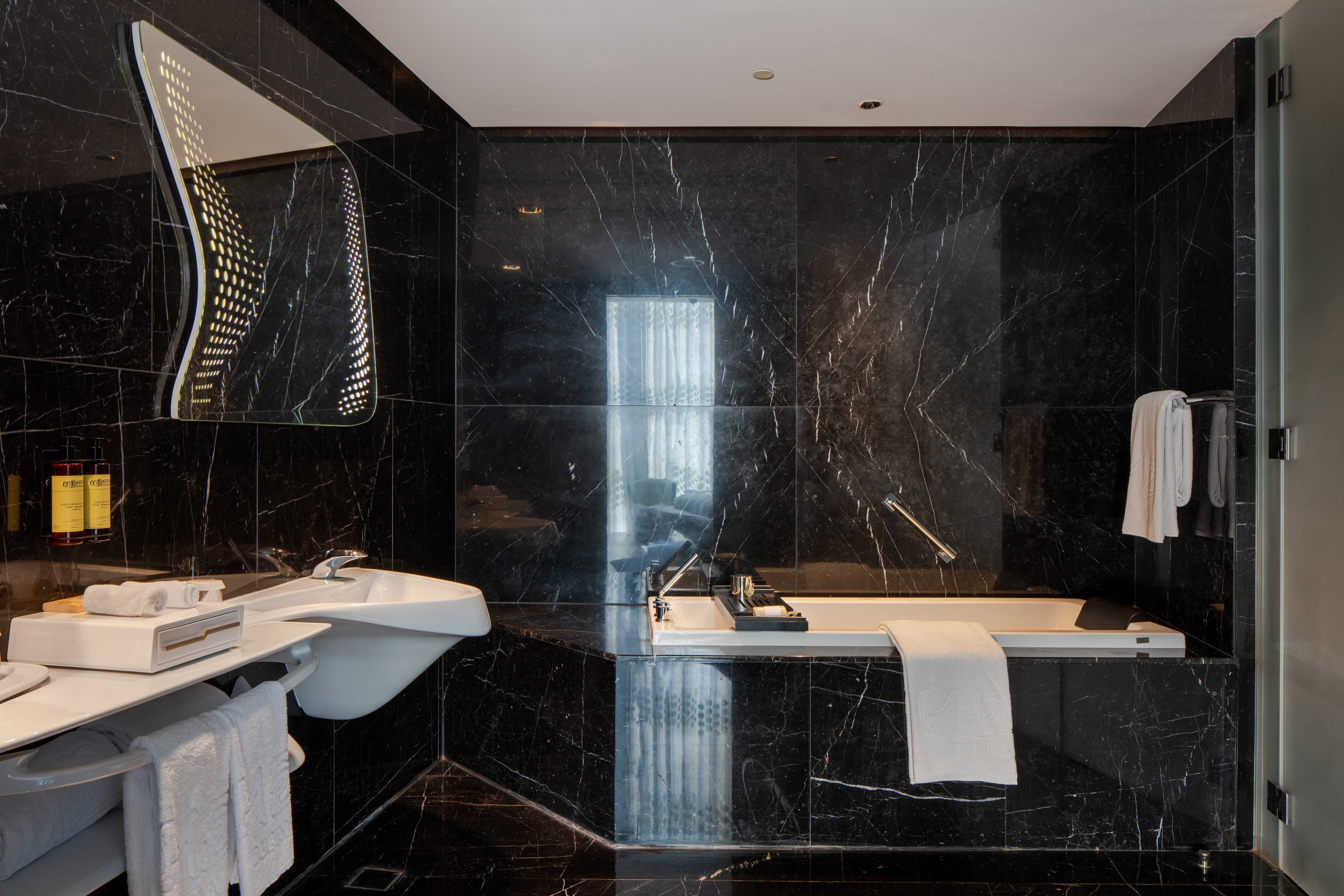 Luxury black marble bathroom with modern sink, bathtub, and illuminated mirror.