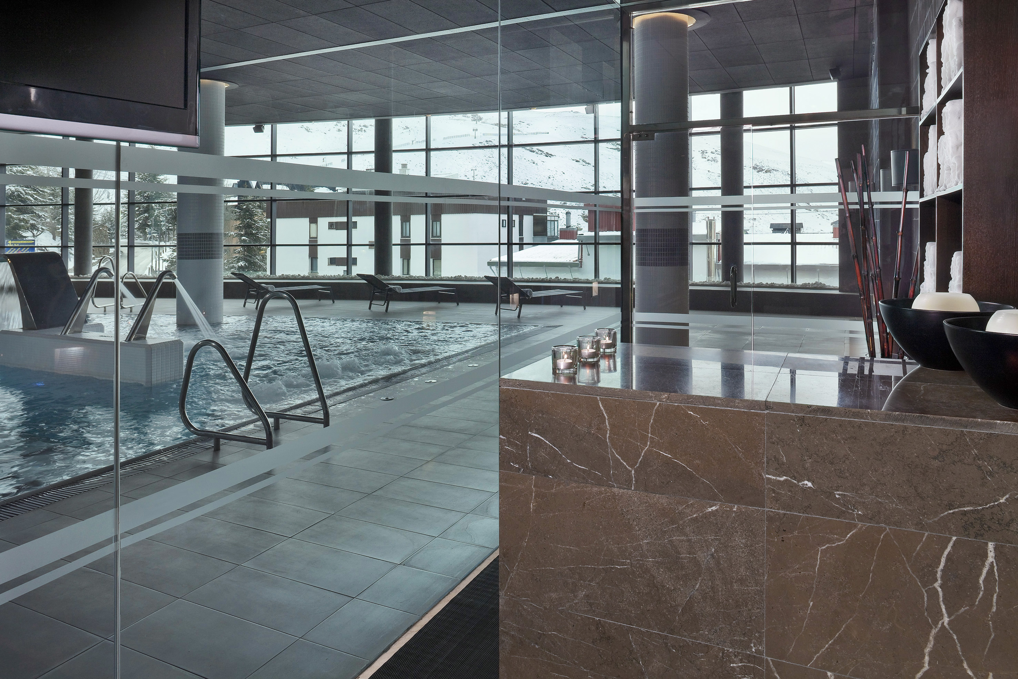 Modern indoor pool, spa, and wellness area with snowy mountain views.