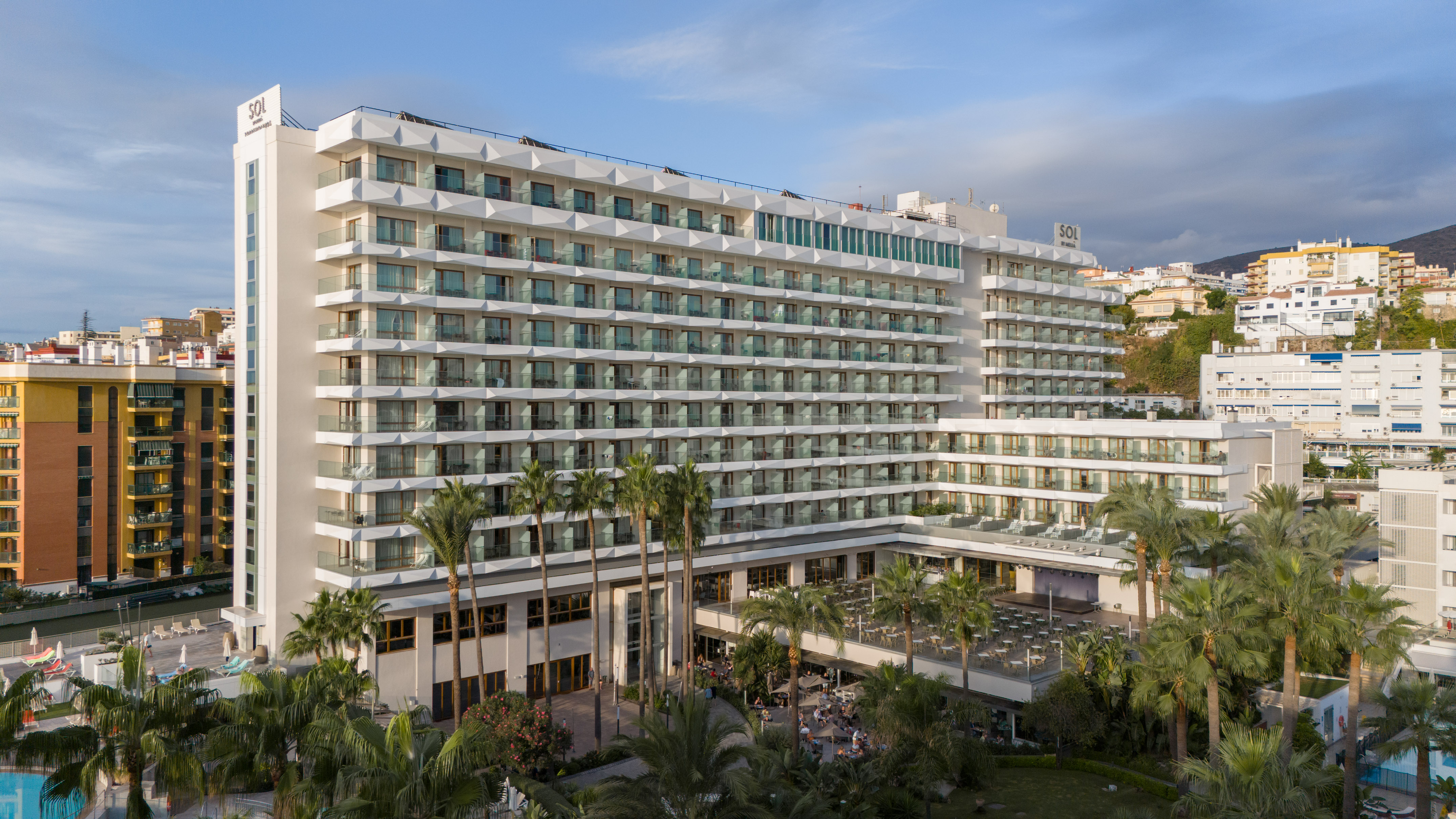 Modern Sol hotel with balconies, palm trees, outdoor dining, and a pool.