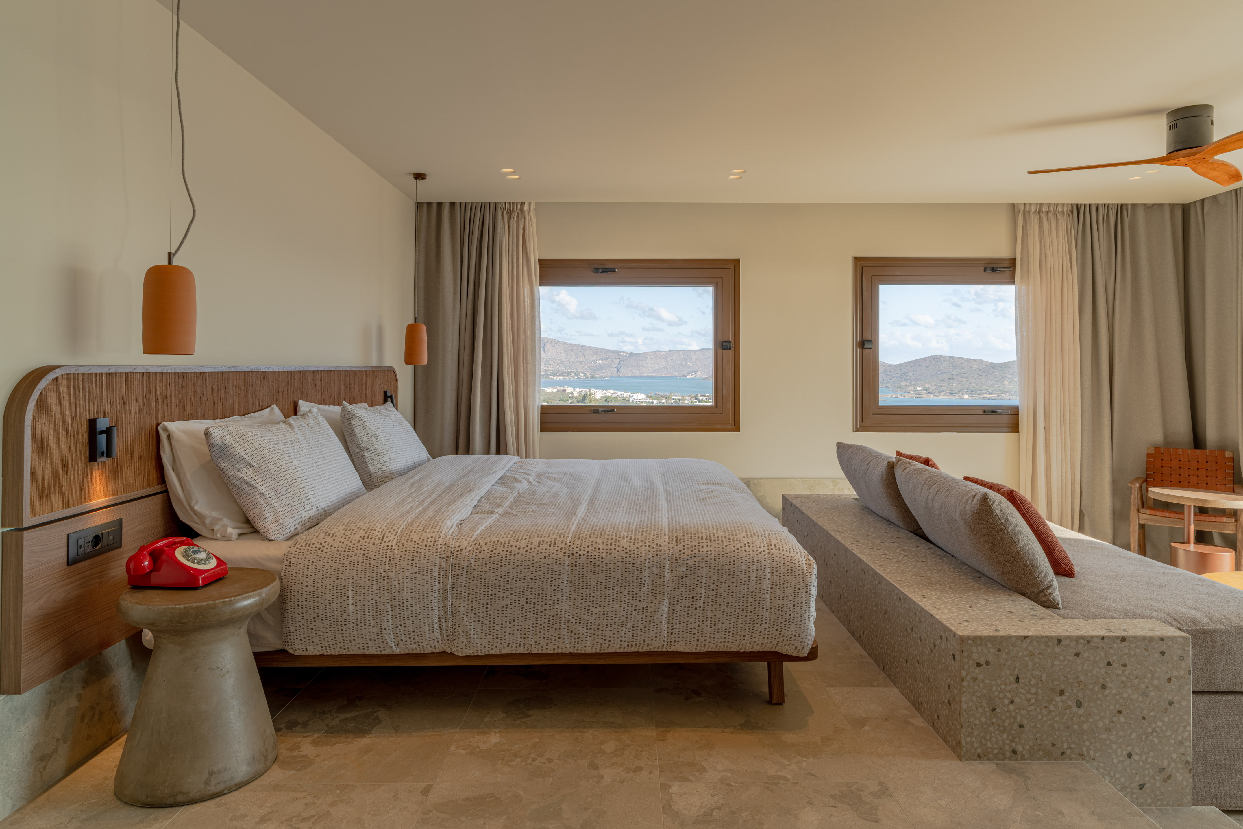 Coastal hotel bedroom with sea view, modern bed, and stylish concrete lounge.