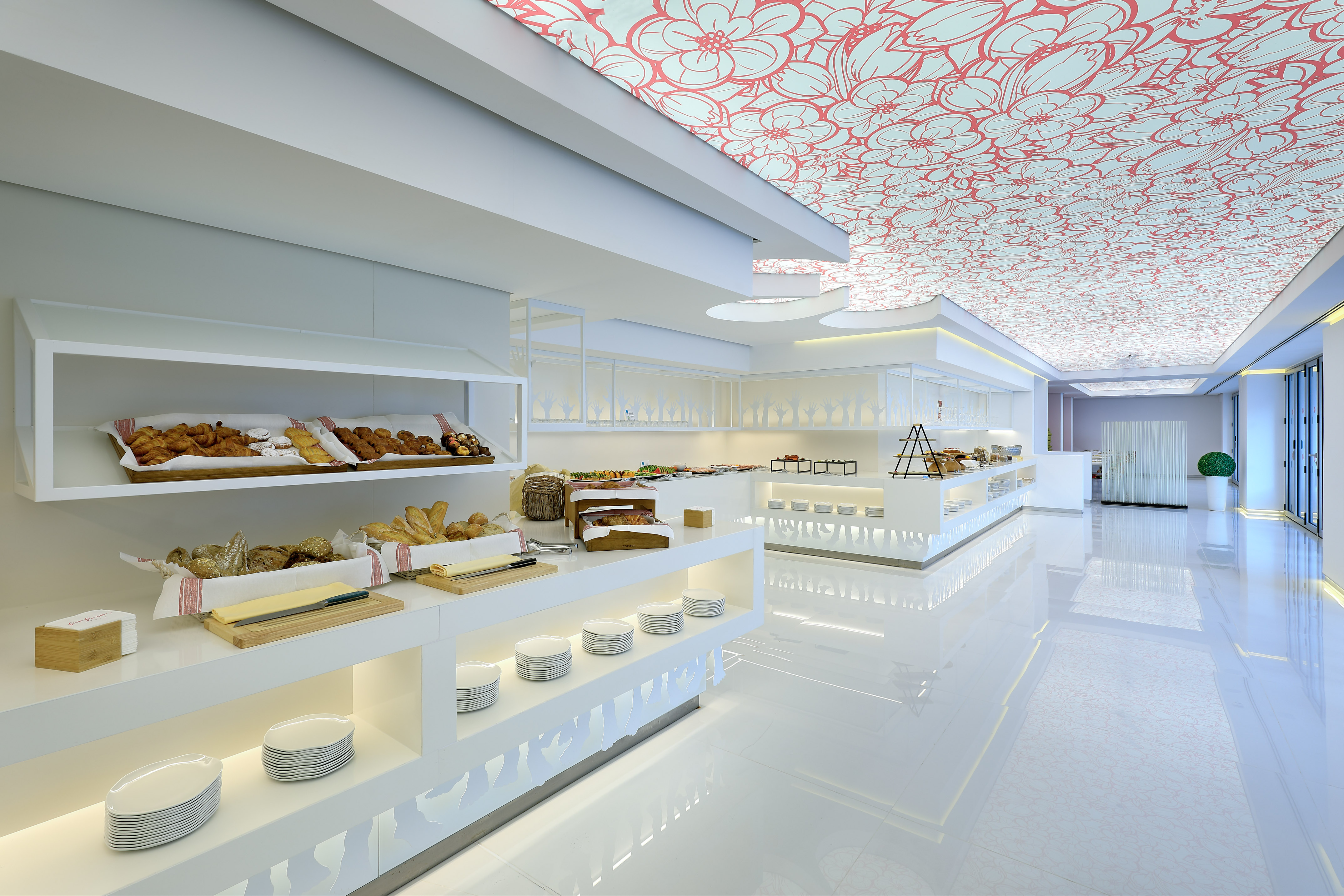 Modern hotel buffet breakfast with pastries, bread, and red floral ceiling.