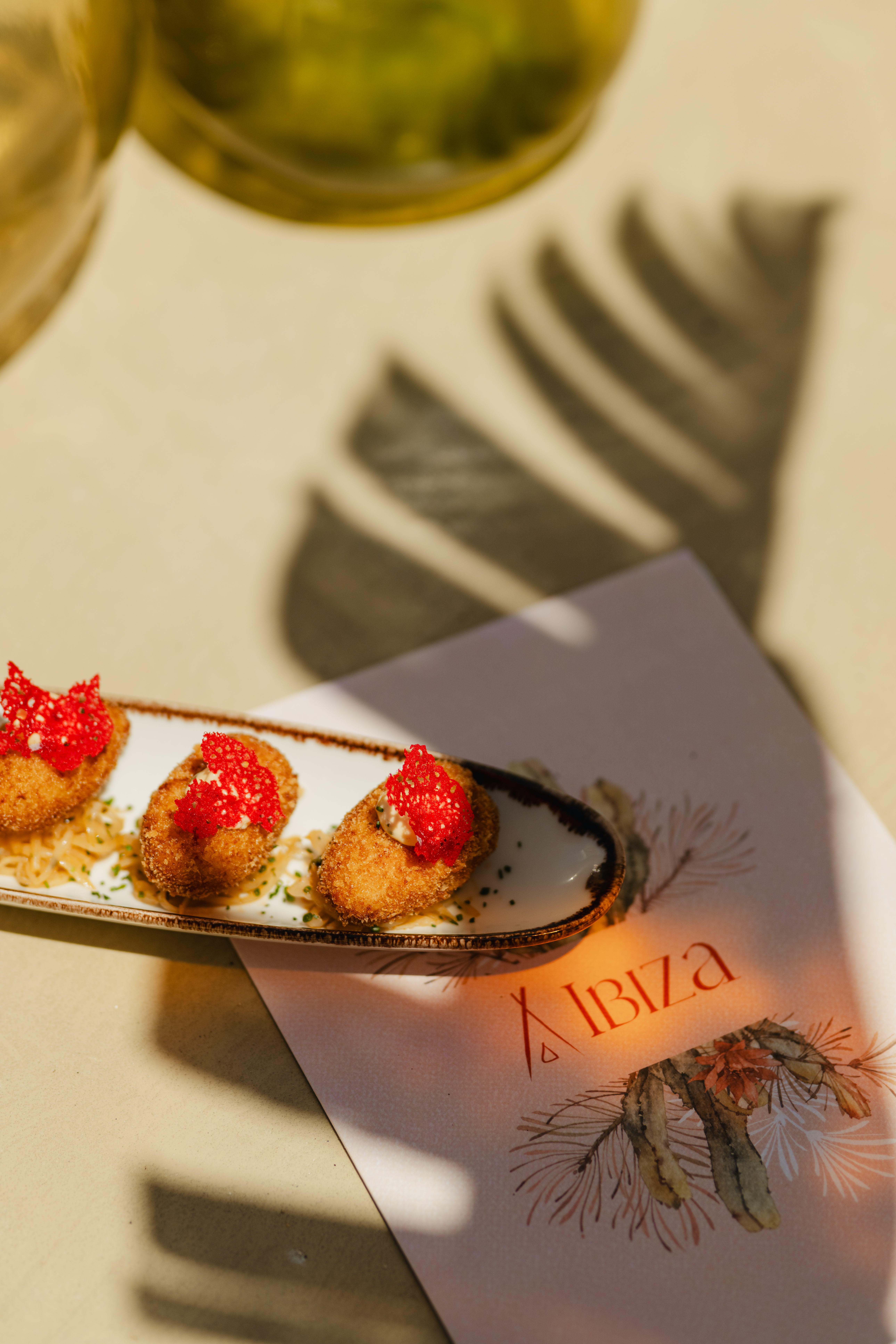 Golden croquettes with red garnish on an Ibiza menu, sunlit table.