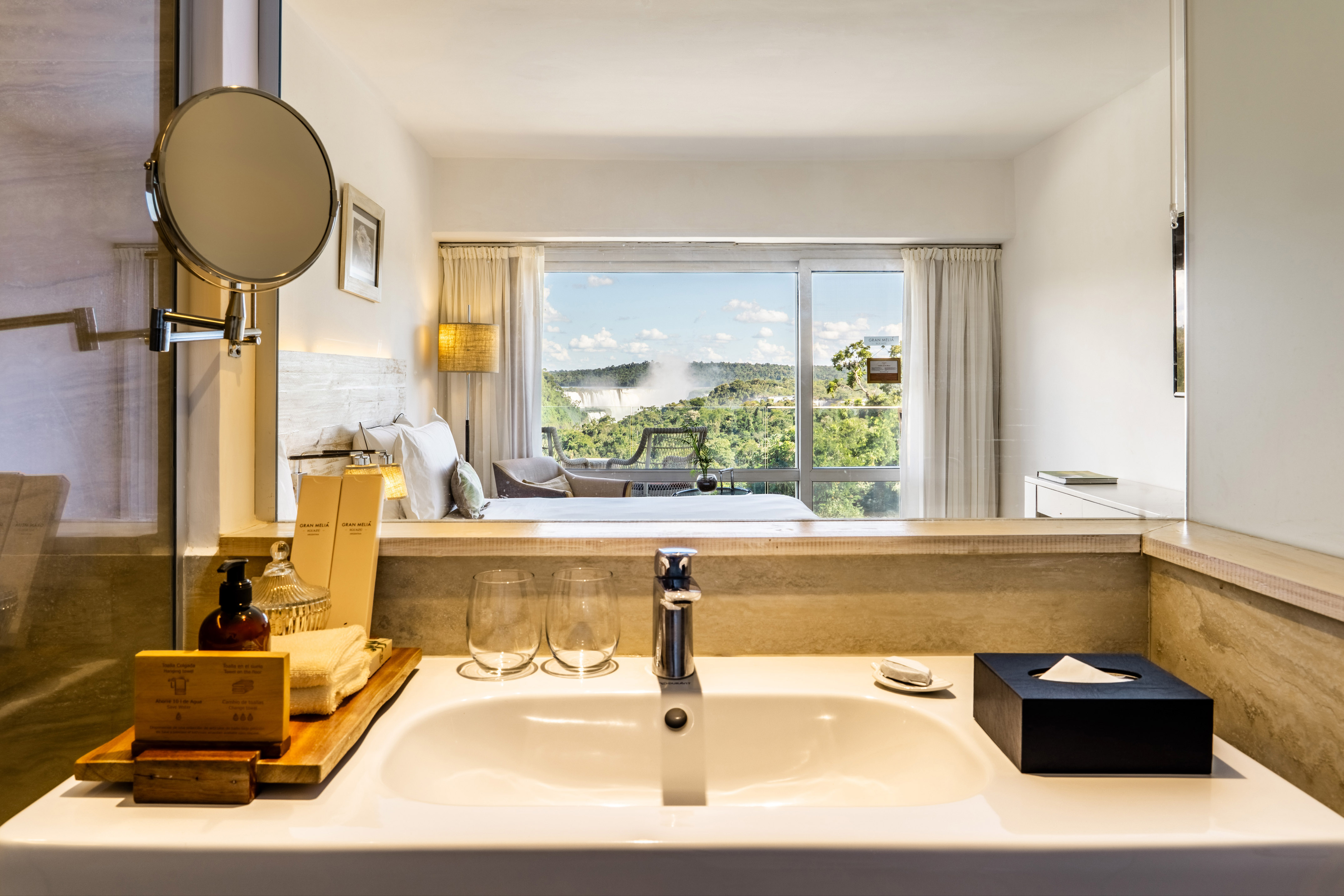 Luxury hotel suite with bathroom vanity and panoramic Iguazu Falls view.