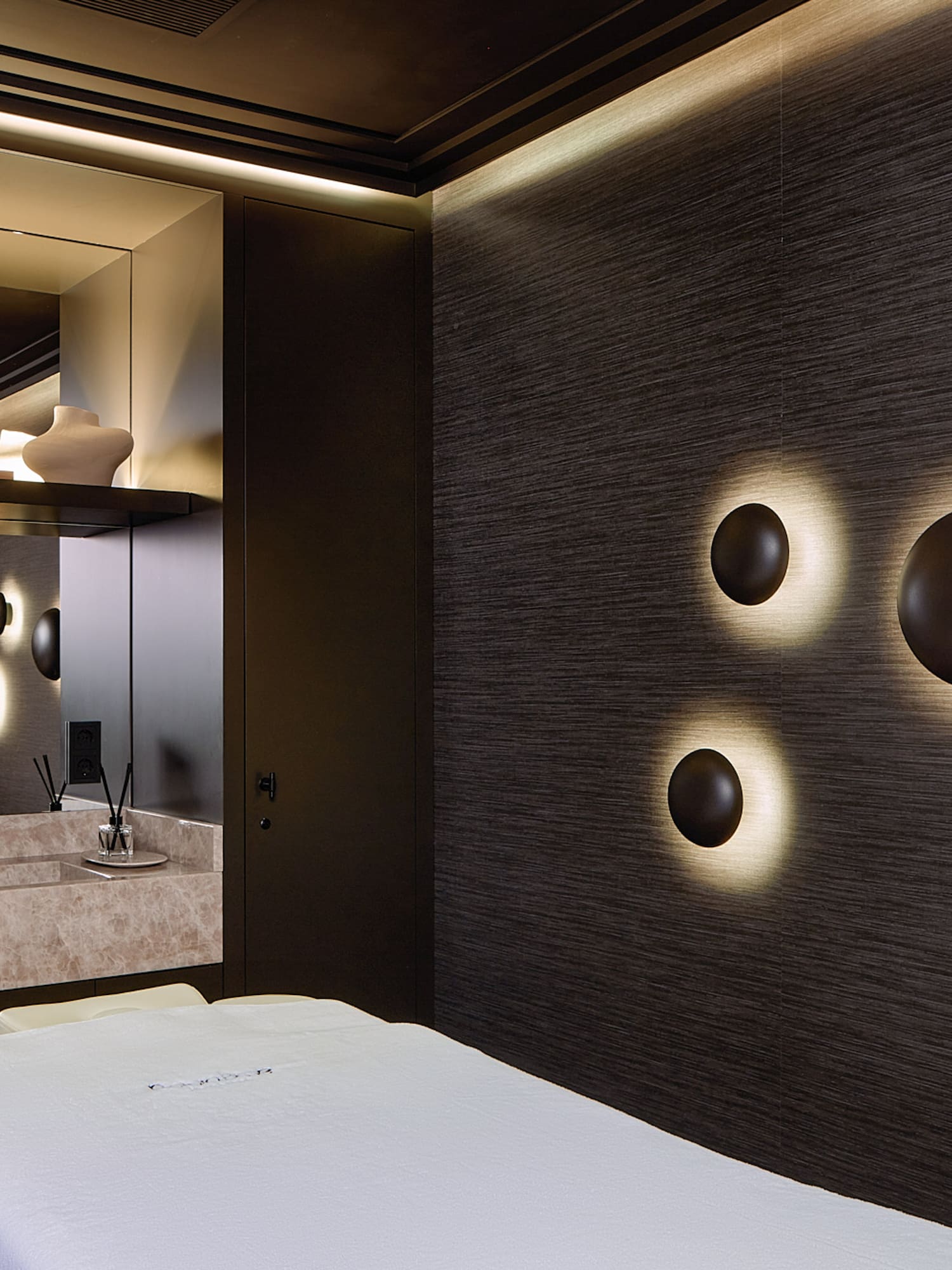 Dark luxury spa treatment room with sconce lights, marble vanity, and massage bed.