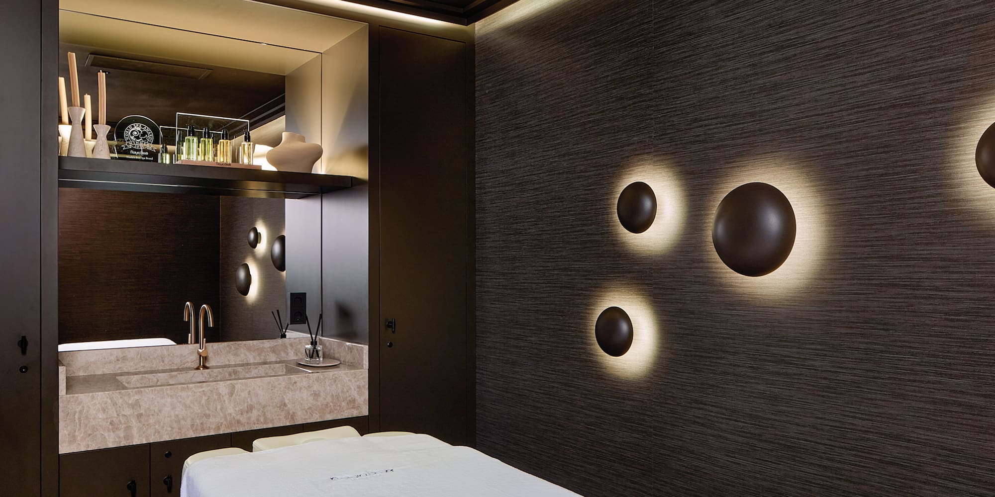 Spa moderno: camilla de masaje, lavabo de mármol y luces de pared.