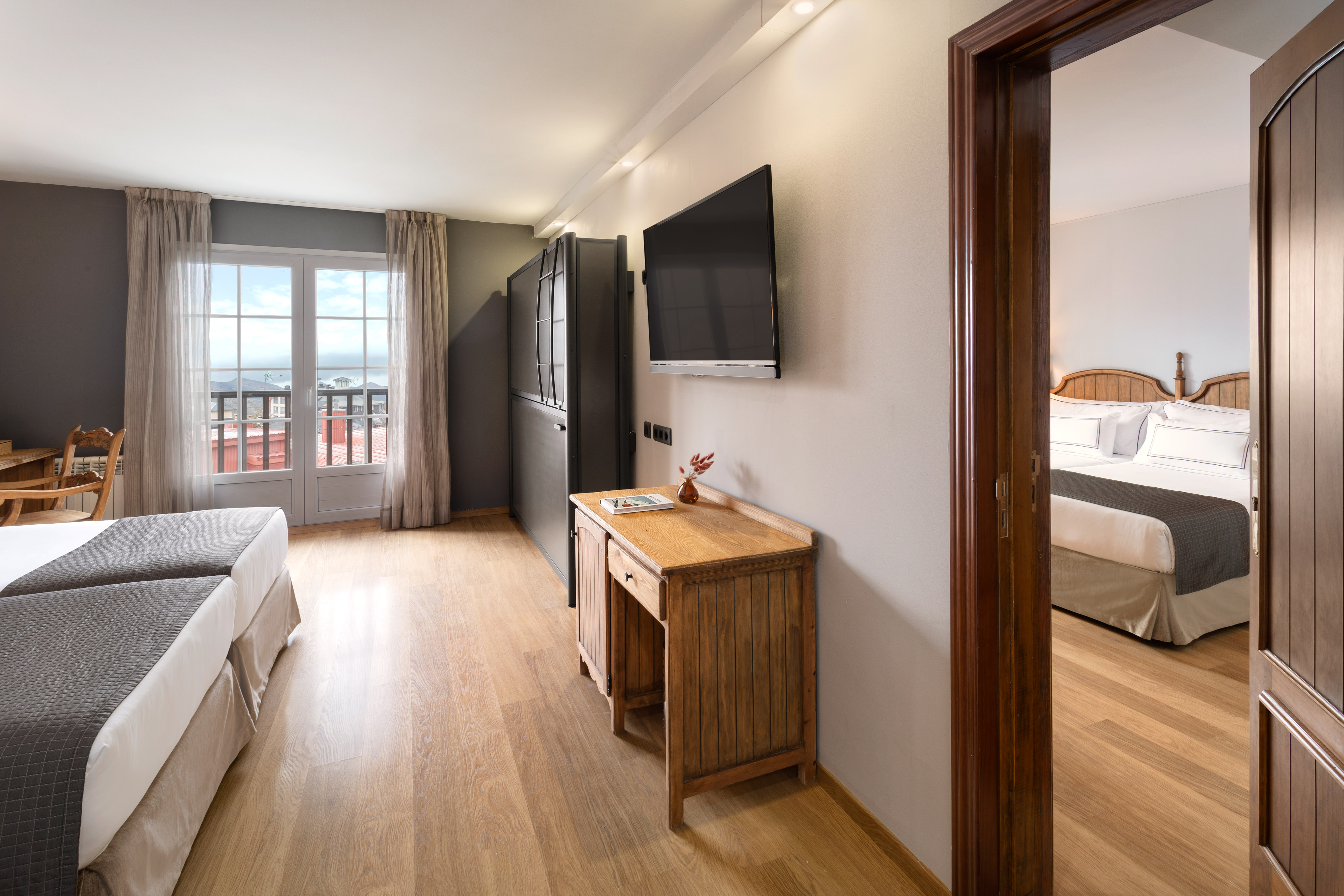 Hotel room with twin beds, balcony ocean view, wooden floor, and connecting door.