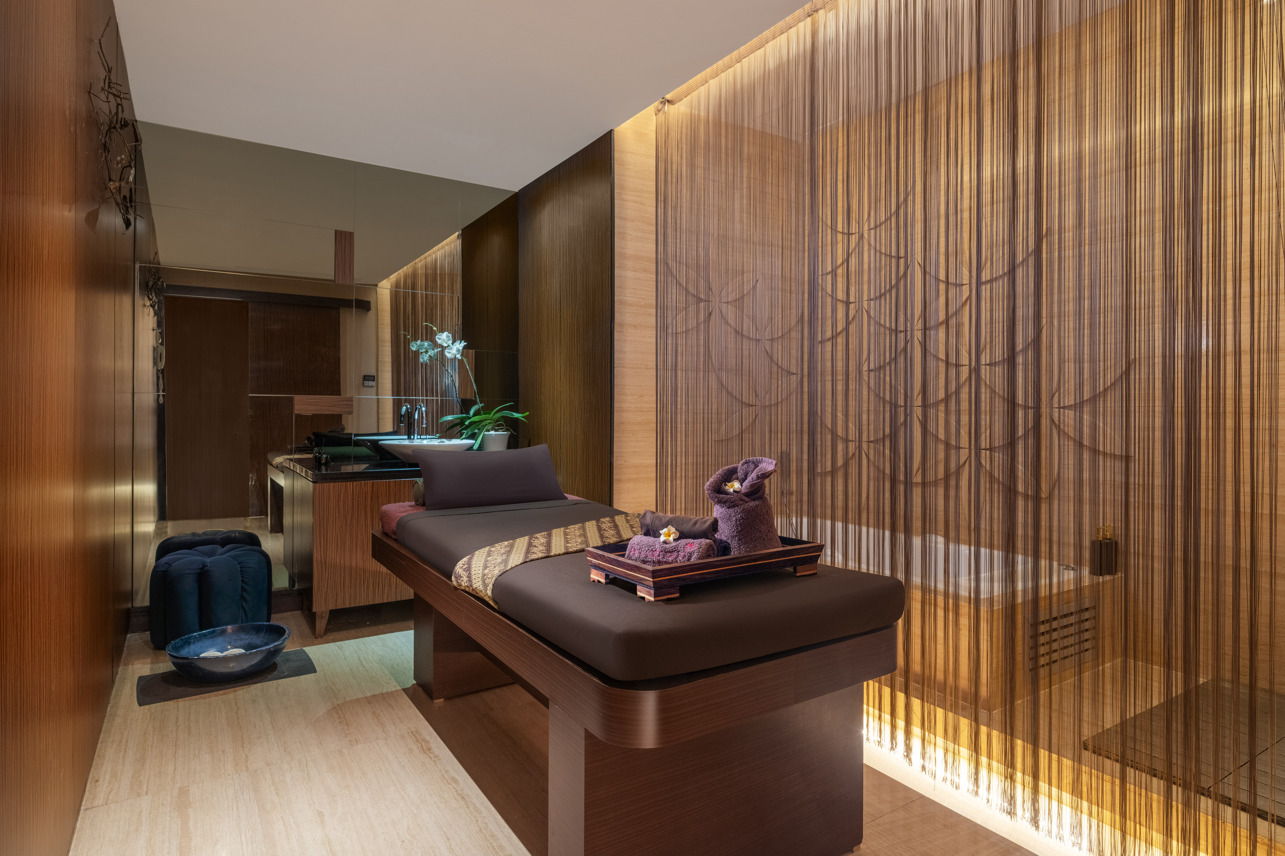 Serene spa room with massage bed, elegant wood, string curtains, and bathtub.