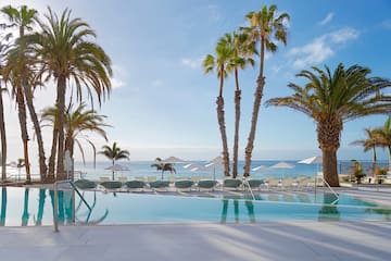 a pool with palm trees and umbrellas by the water