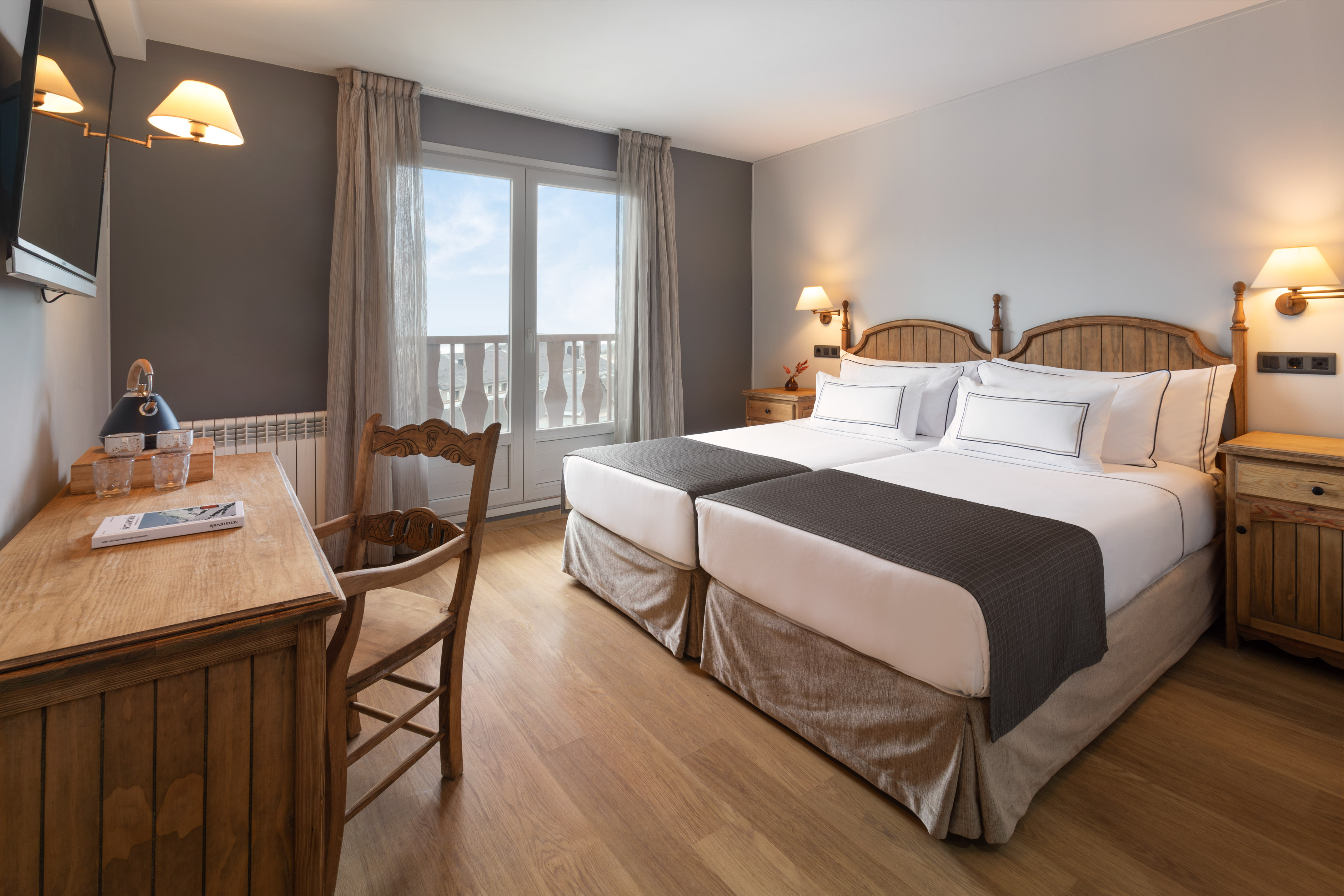 Hotel room with twin beds, wooden furniture, and a balcony view.