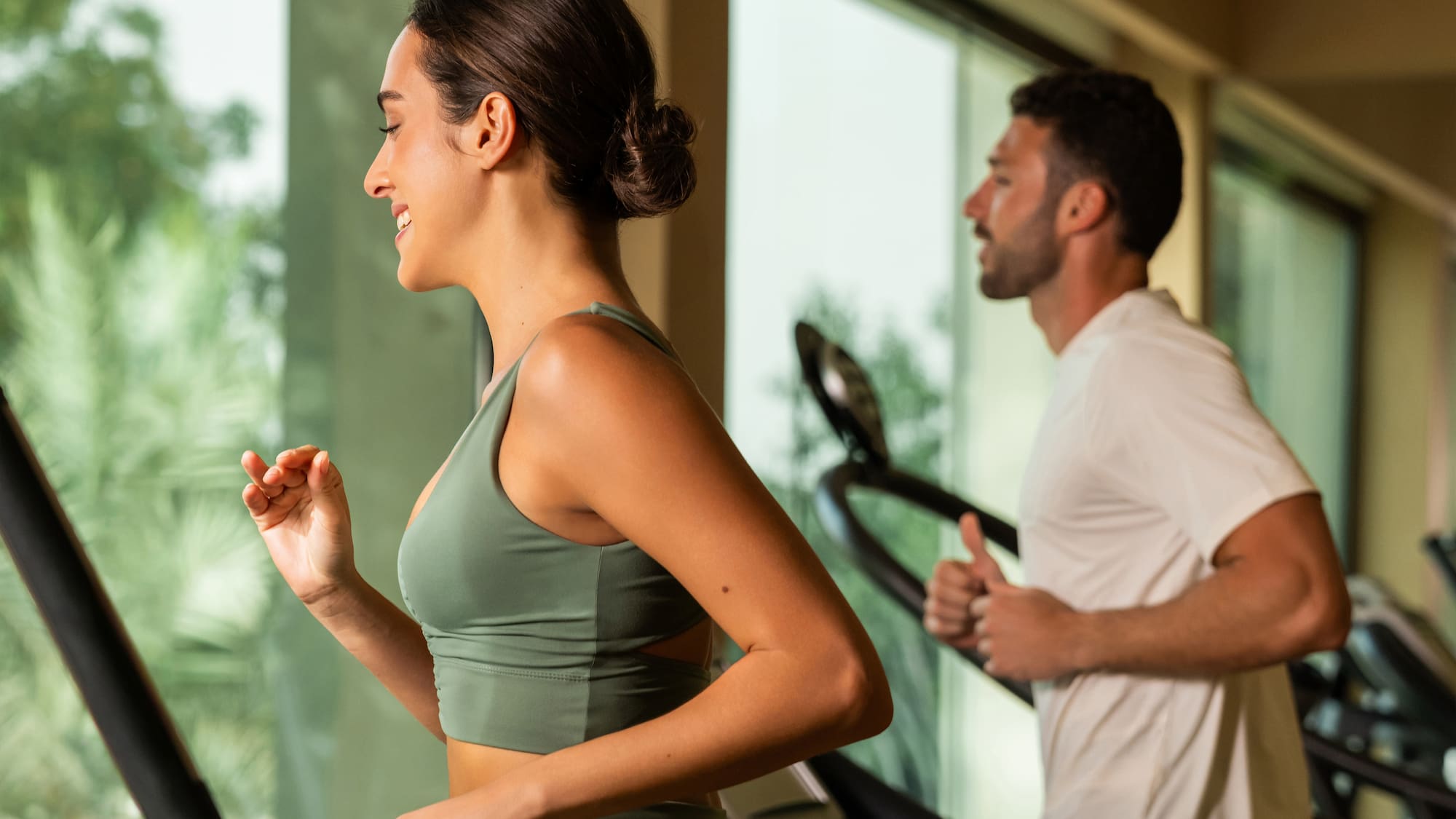 Smiling woman and man running on treadmills in a fitness gym.