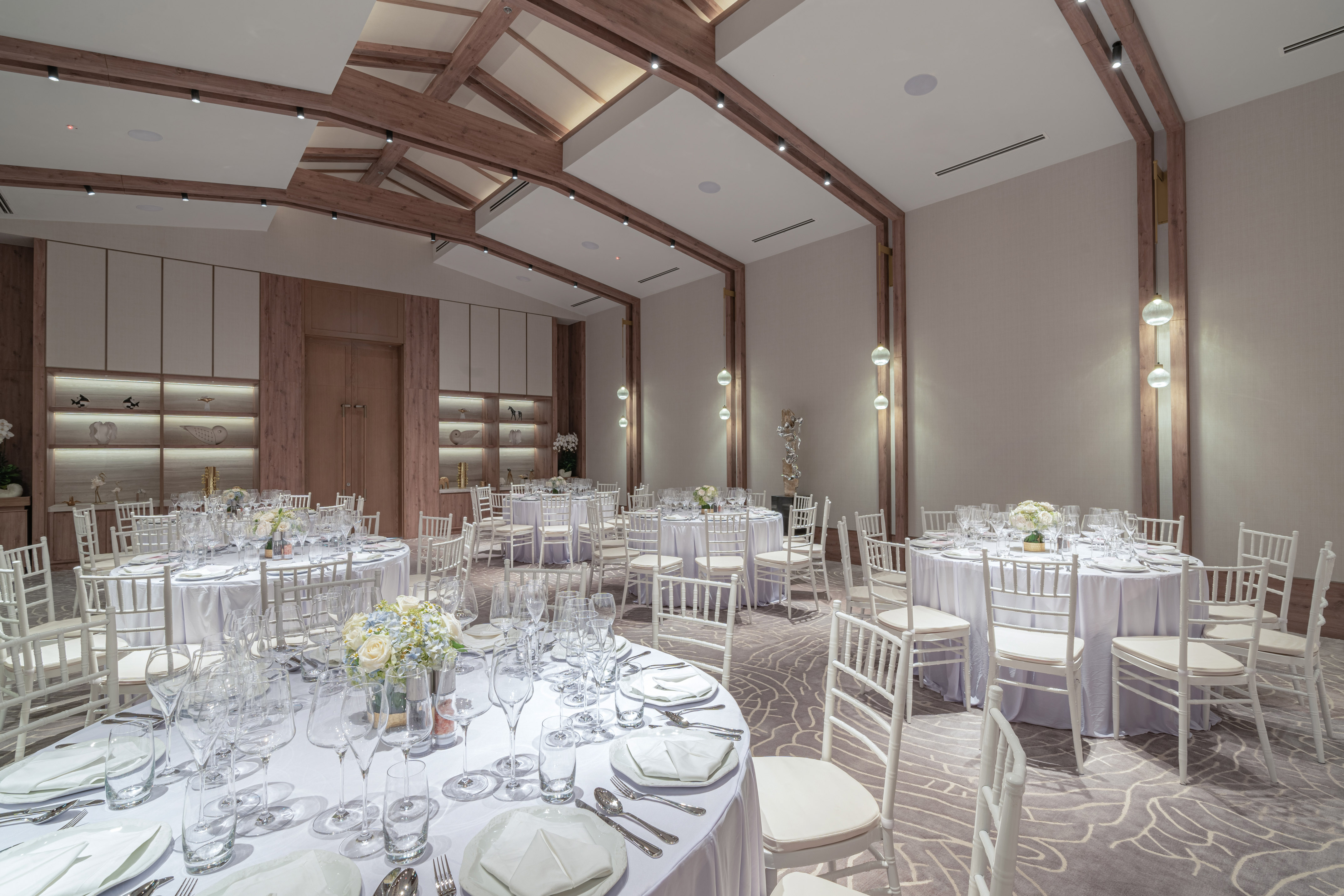 Elegant event space with round dining tables, white chairs, and modern decor.