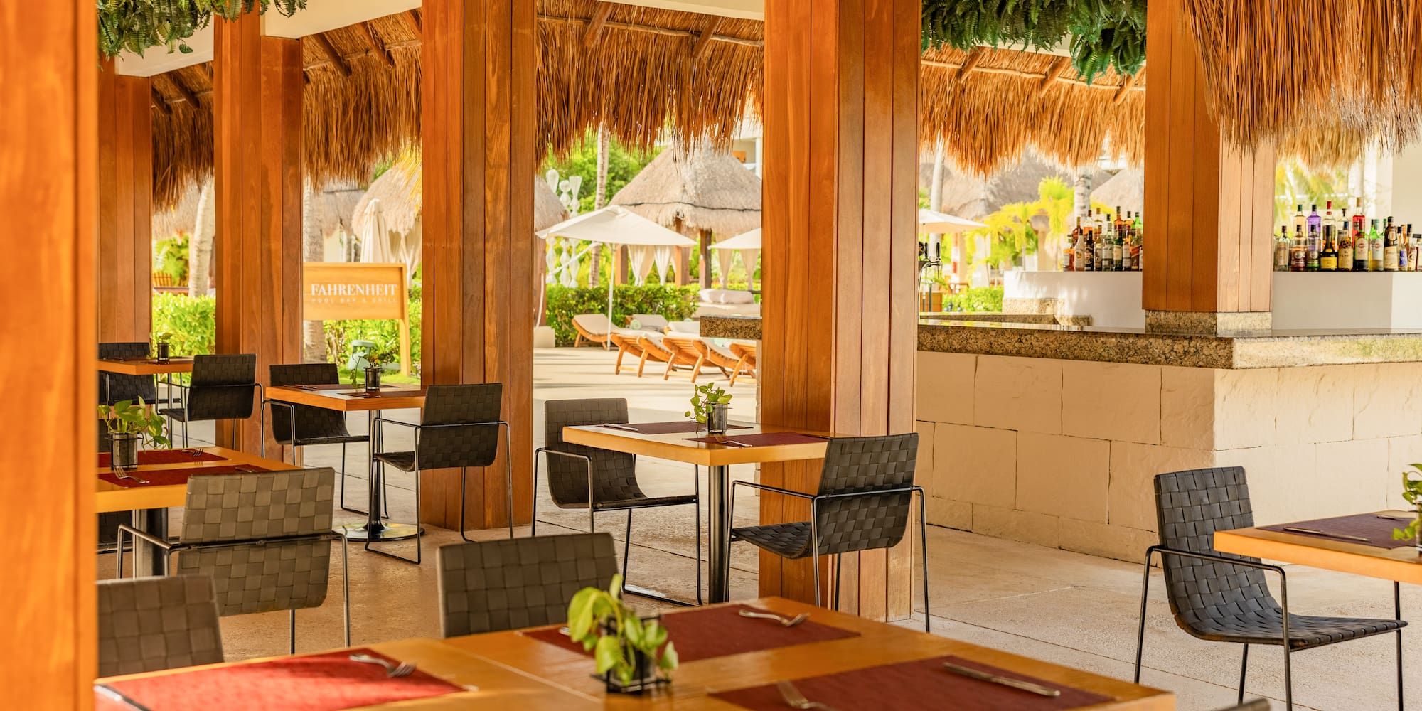 Outdoor resort dining with wooden tables, palapa roof, and full bar.