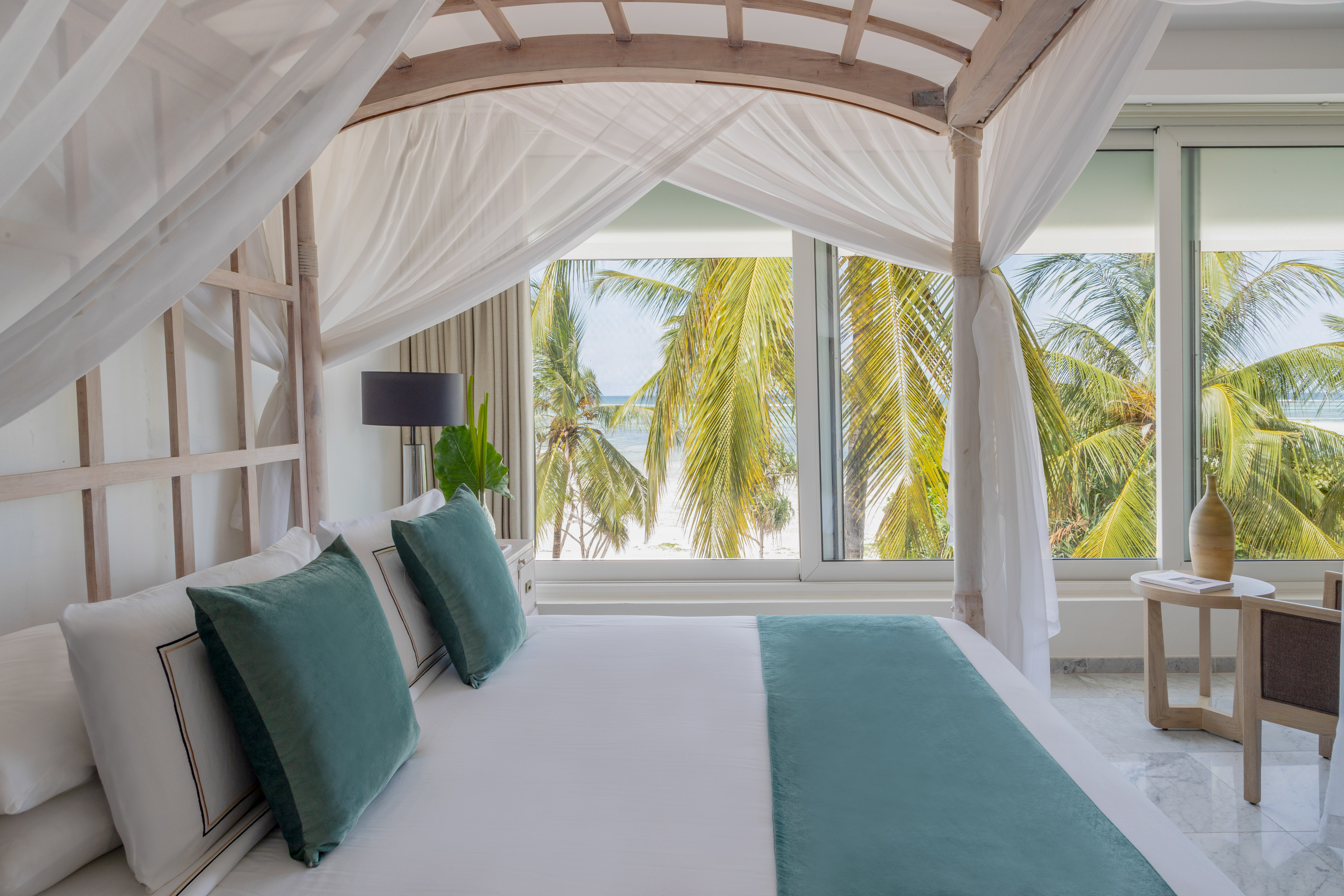 Luxury hotel room with four-poster bed, ocean view, and palm trees.