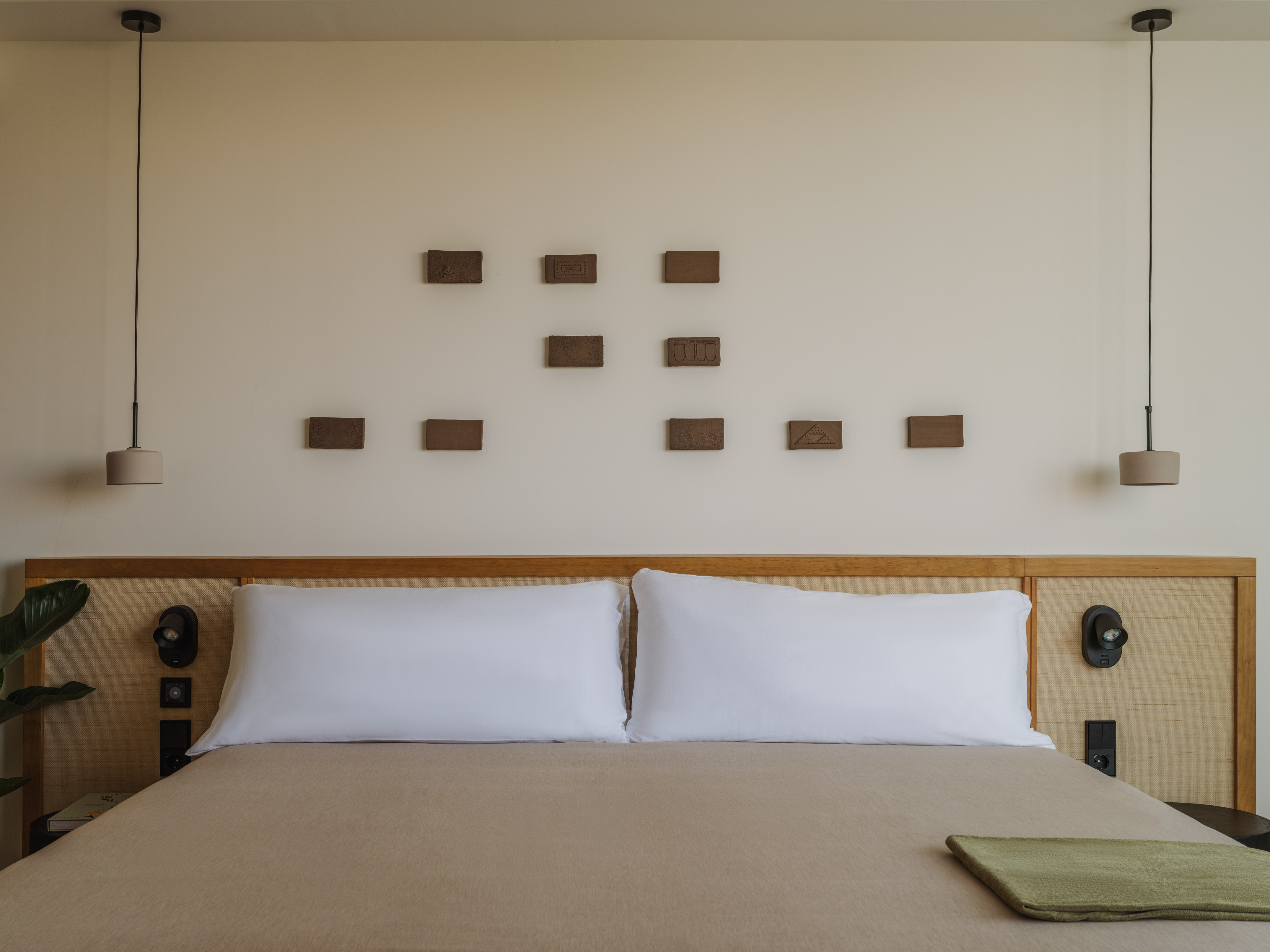 Modern bedroom with wooden headboard, beige bed, pendant lights, and wall art.