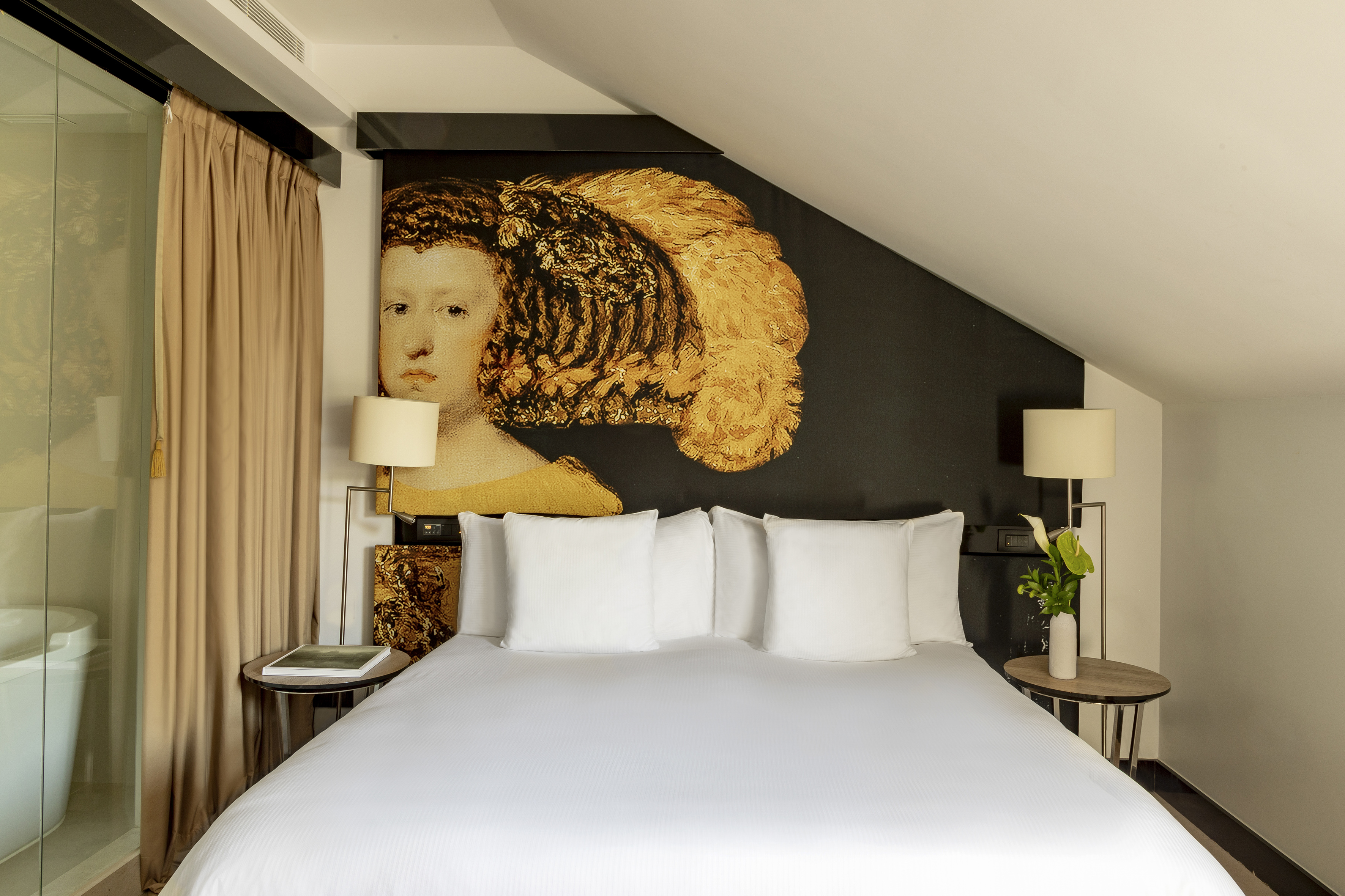 Stylish hotel bedroom with king bed, large classical tapestry, and white bedding.