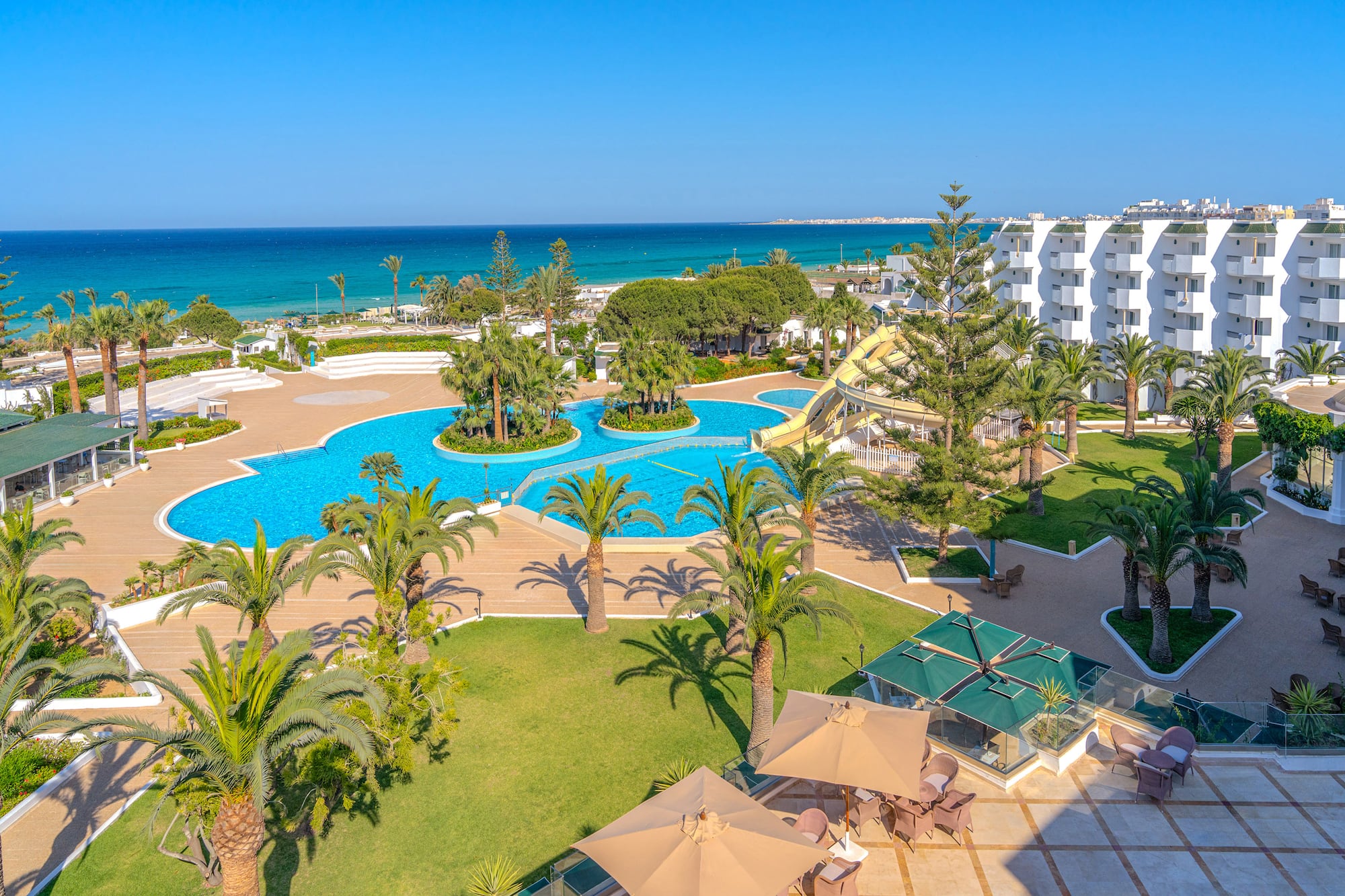 Resort frente al mar con piscinas, tobogán acuático y palmeras.