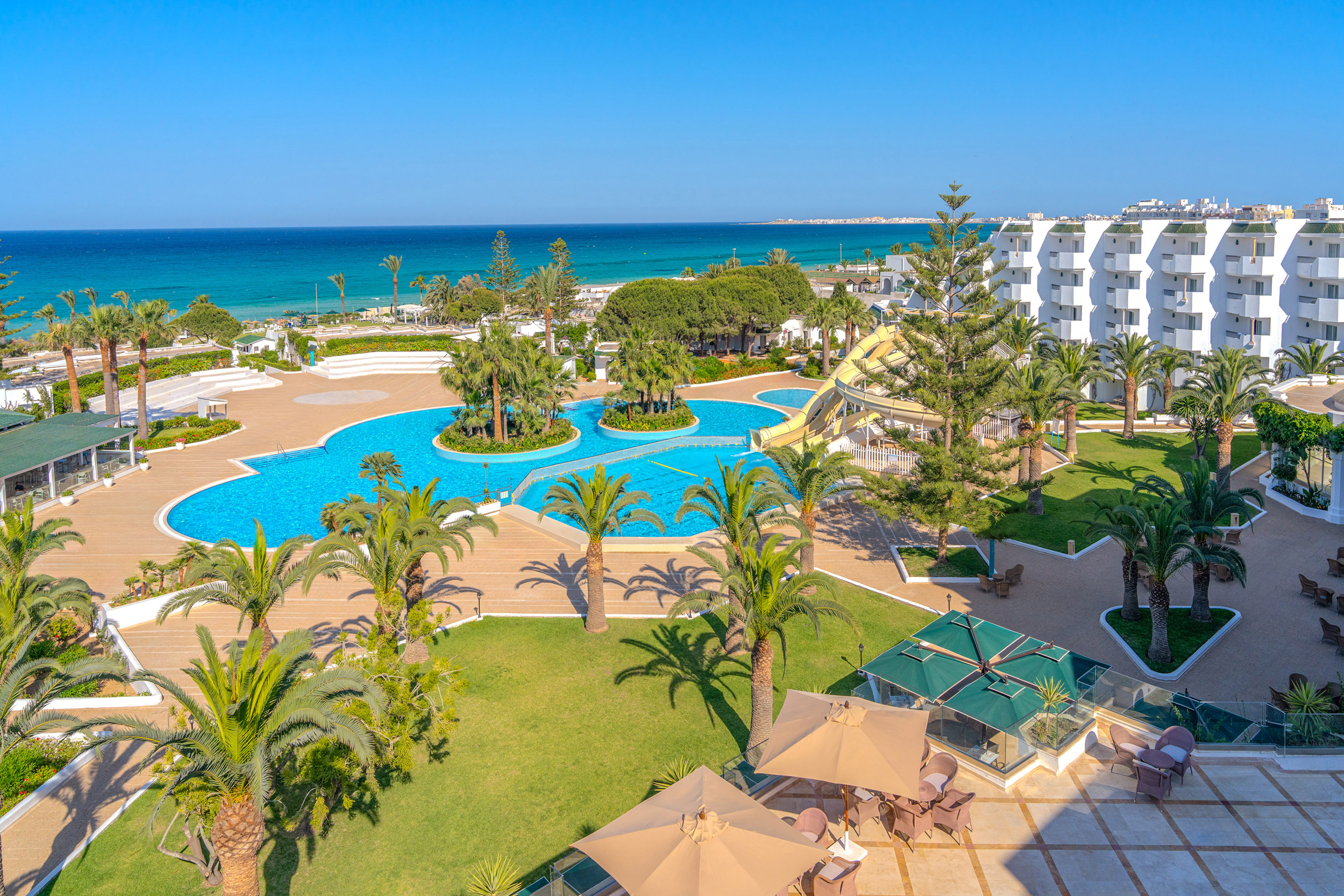 Resort frente al mar con piscinas, tobogán acuático y palmeras.