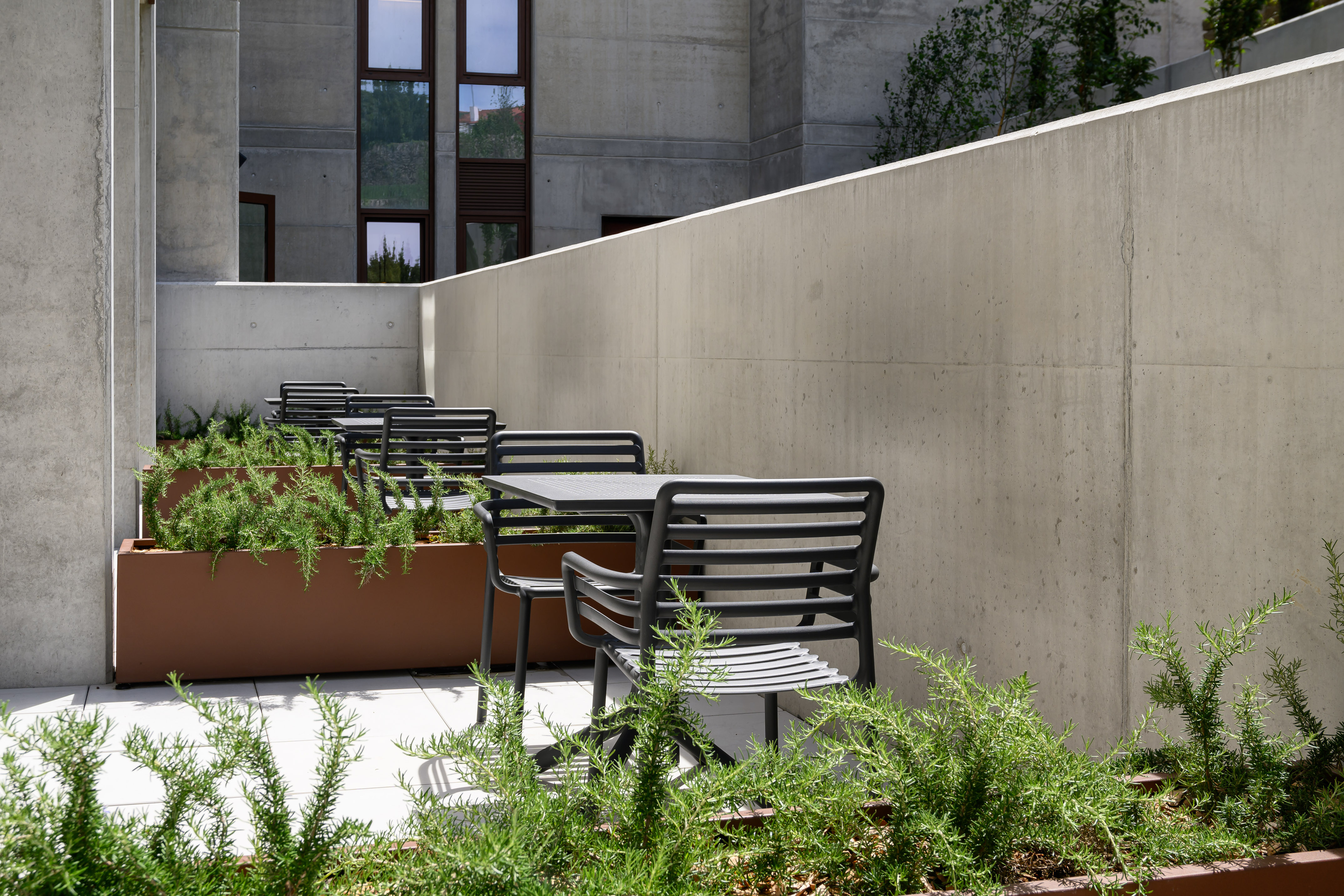 Concrete patio with modern tables, chairs, and lush green plants in planters.