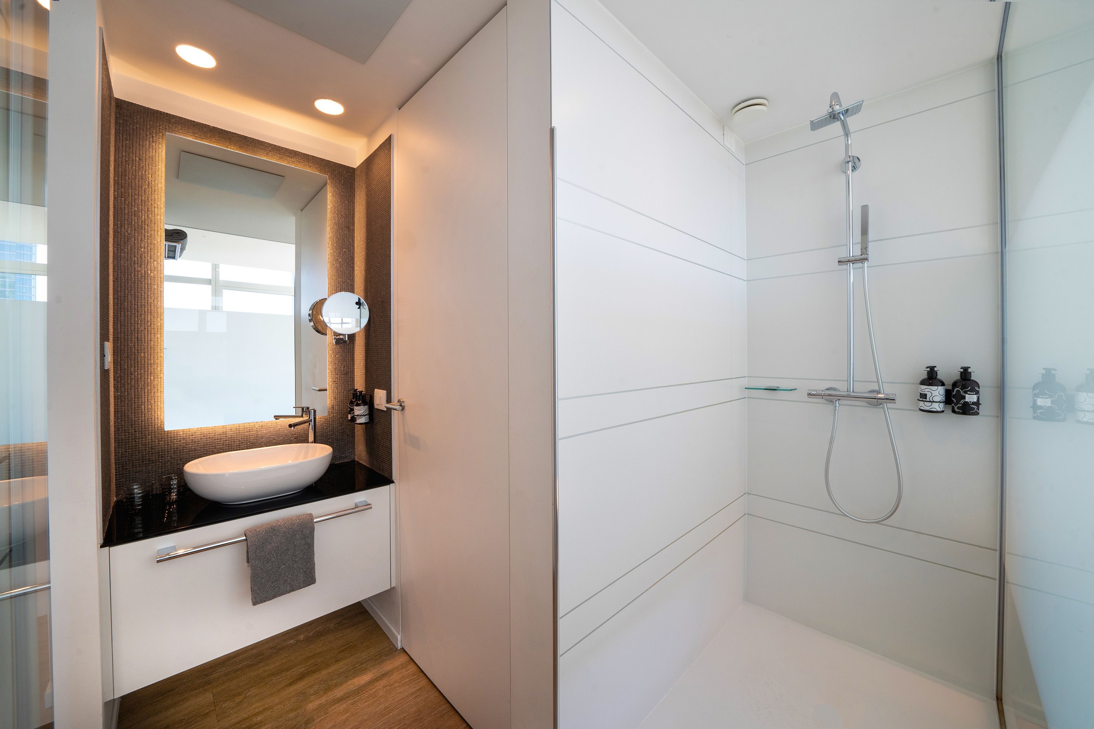 Modern hotel bathroom: vessel sink, backlit mirror, walk-in shower.
