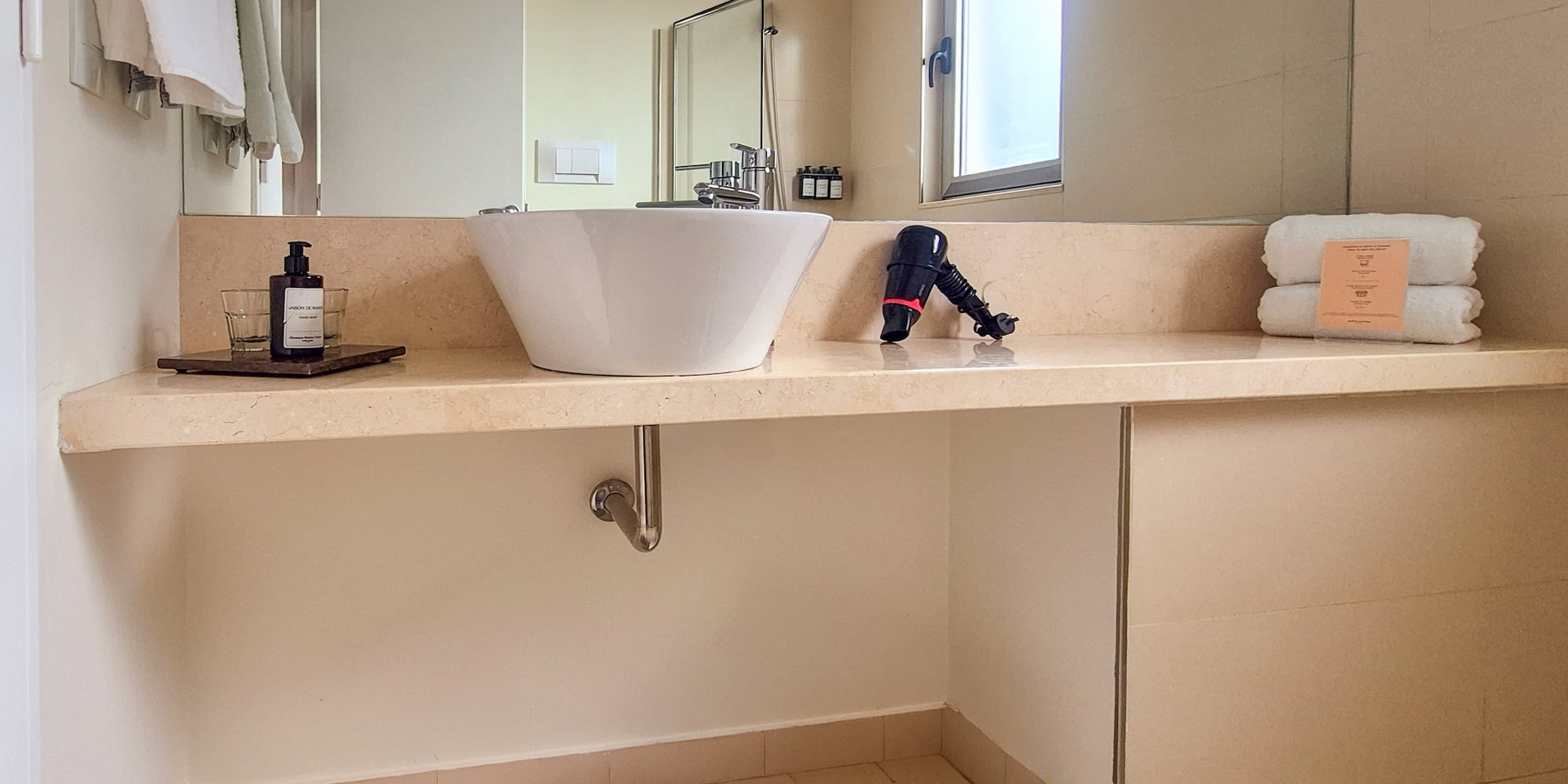 Modern hotel bathroom vanity with vessel sink, toiletries, hairdryer, and towels.