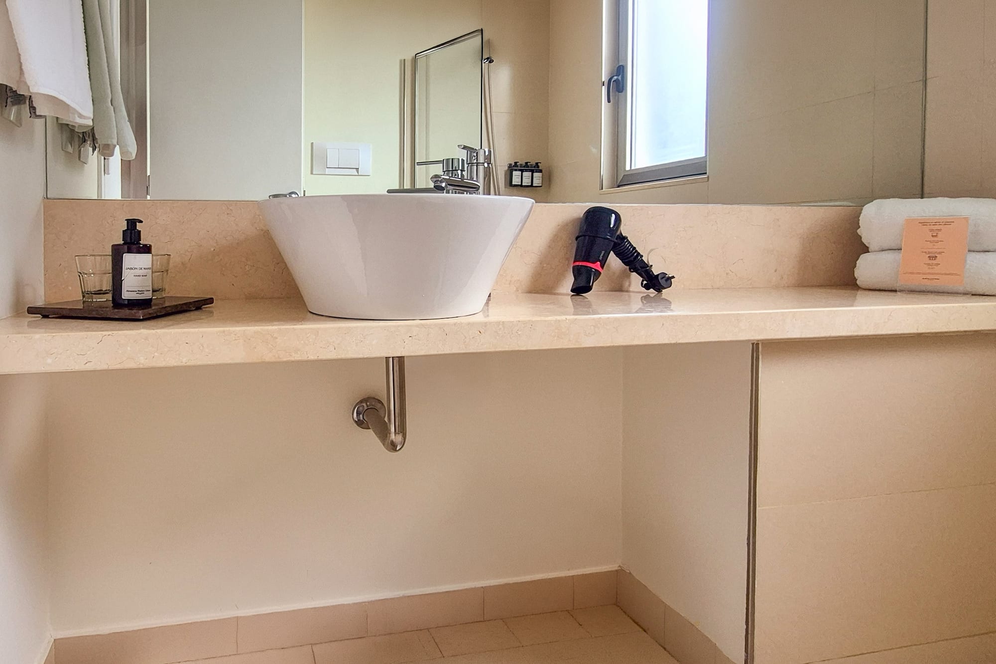 Modern hotel bathroom vanity with vessel sink, toiletries, hairdryer, and towels.