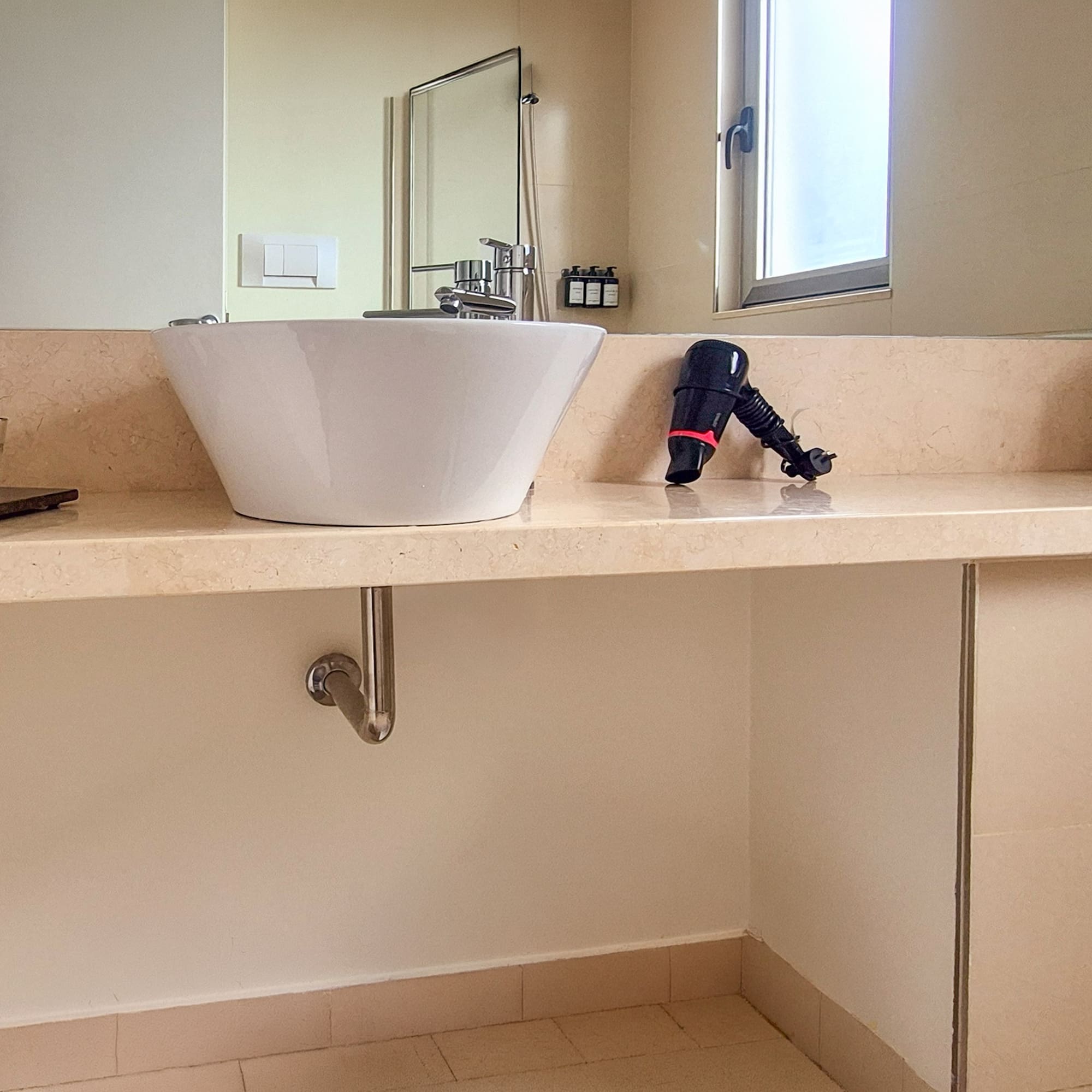 Modern hotel bathroom vanity with vessel sink, toiletries, hairdryer, and towels.
