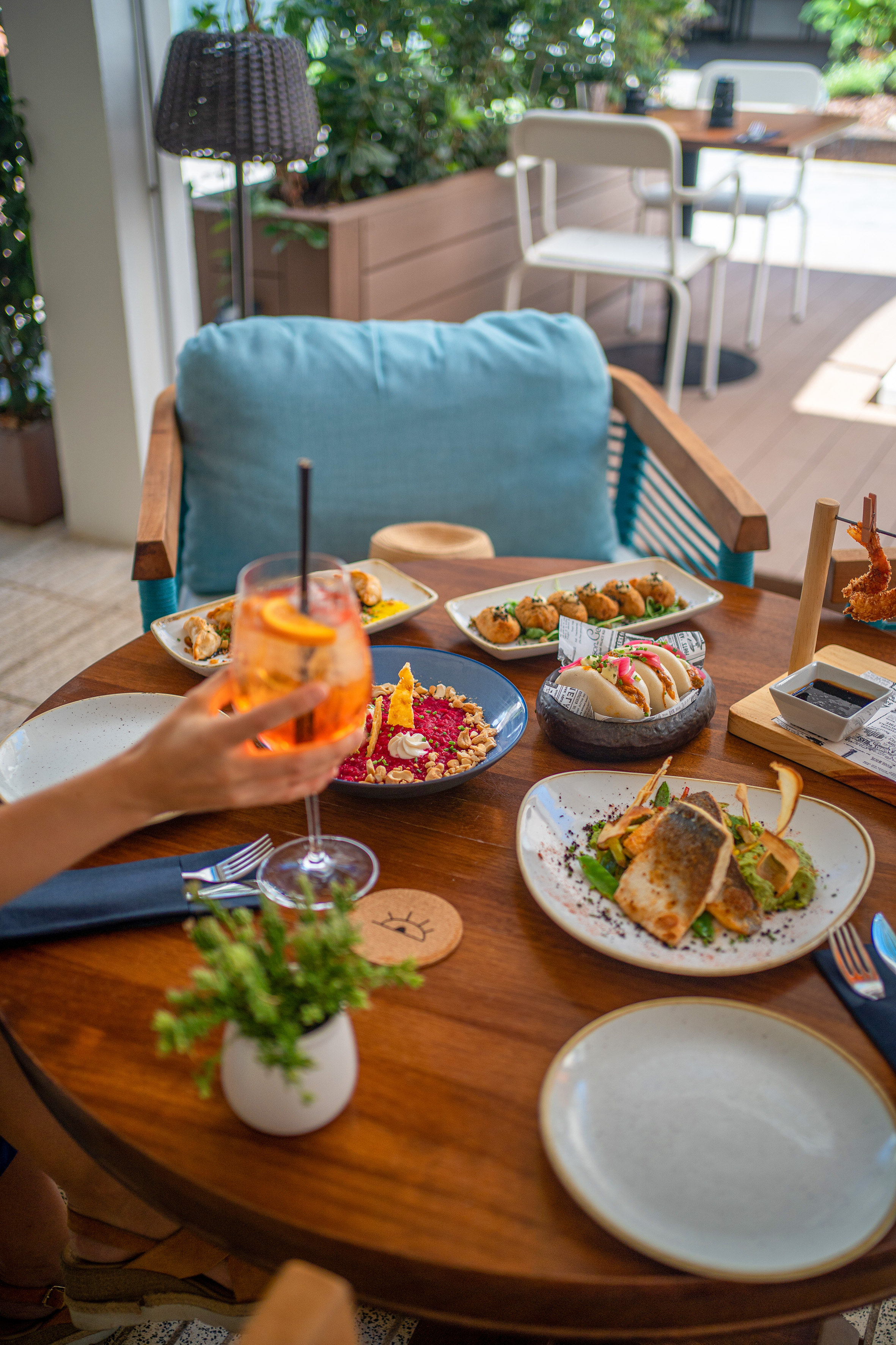 Restaurant dining table with seafood, diverse appetizers, bao buns, and an orange cocktail.