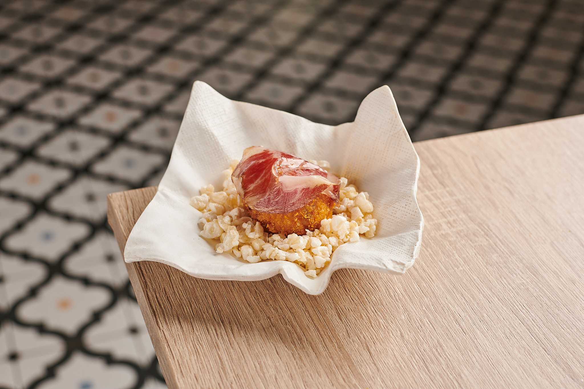 Golden croquette with cured ham and crunchy garnish on a wooden table.
