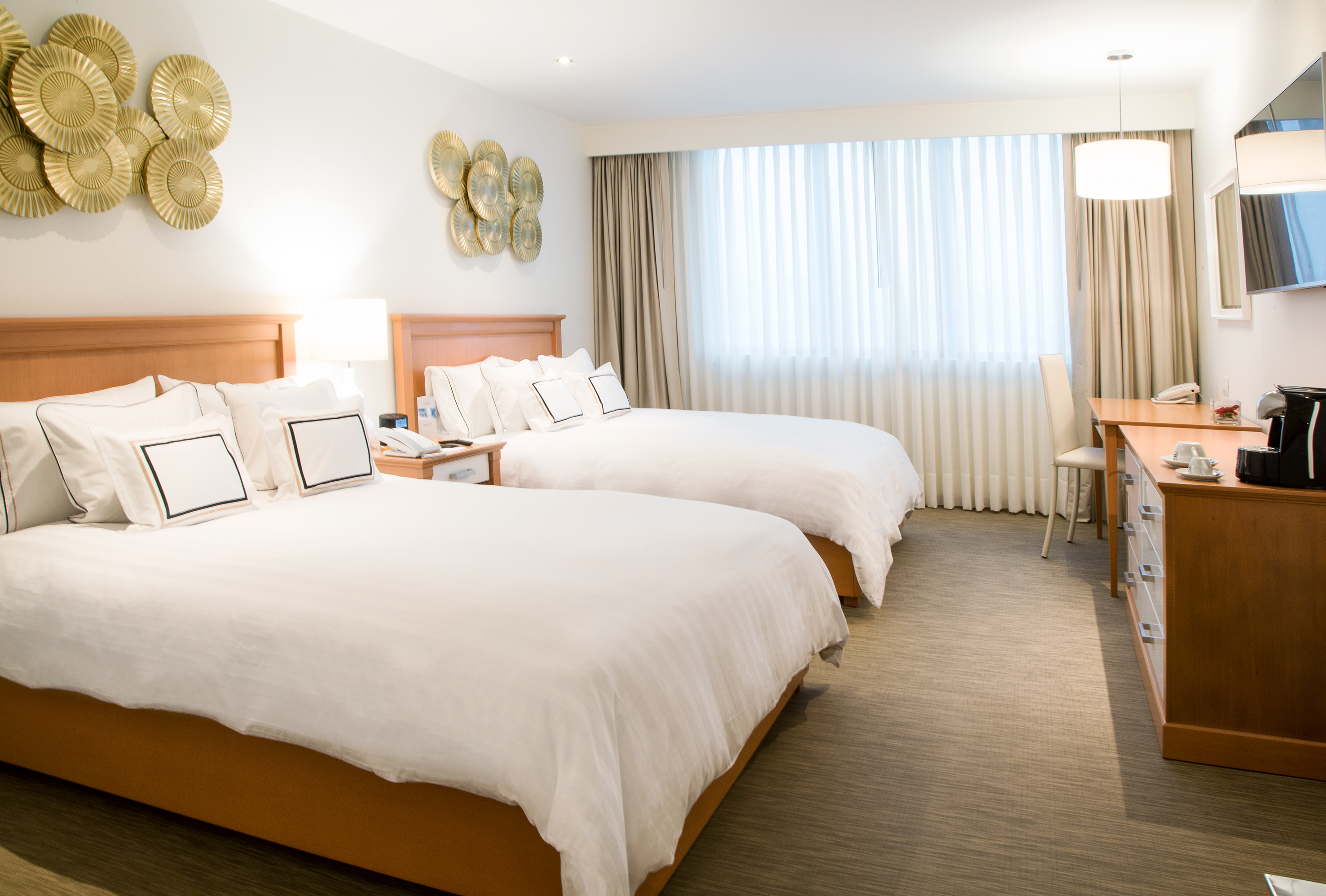 Clean hotel room featuring two queen beds, decorative wall art, and work desk.