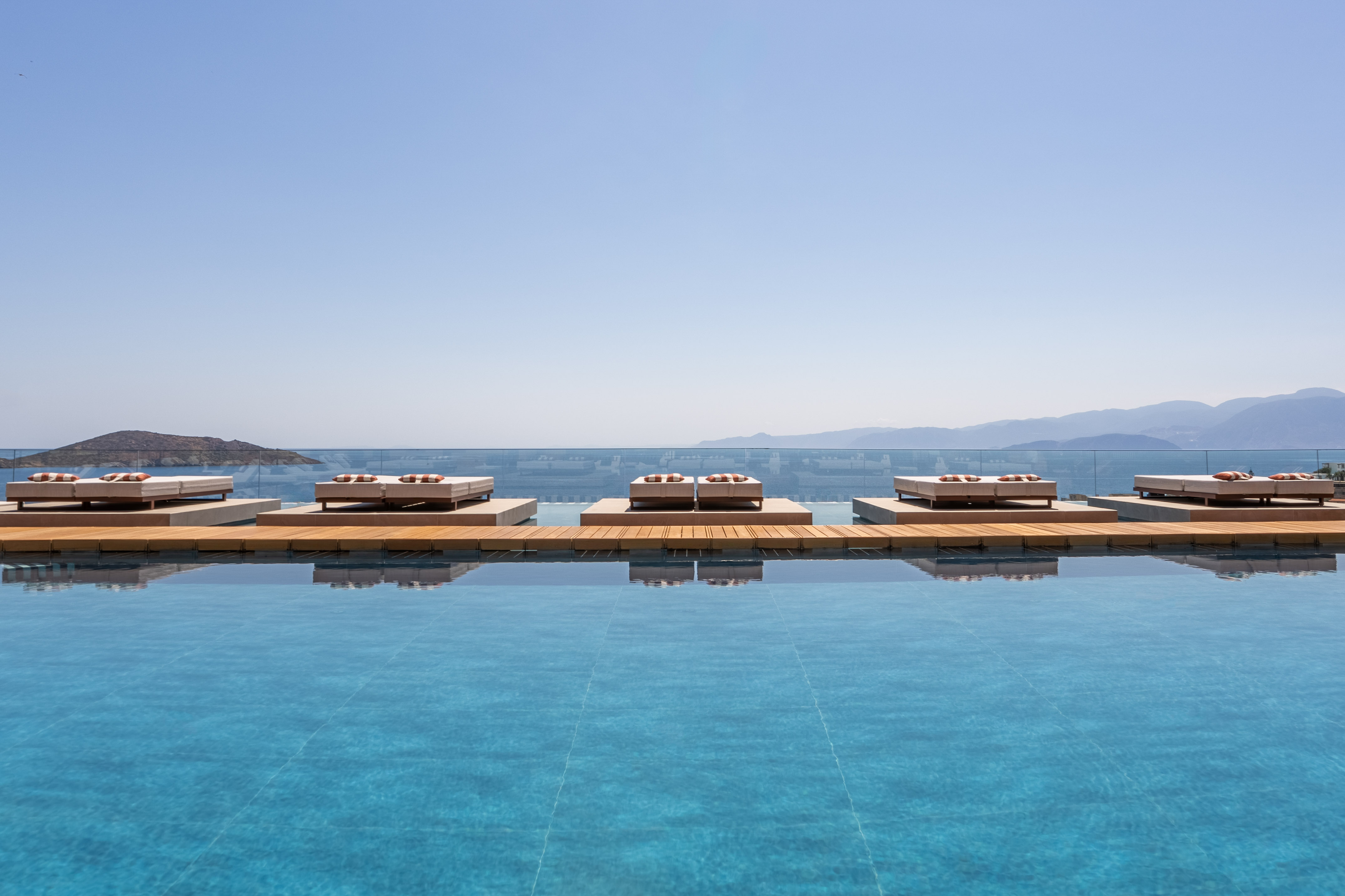 Luxury resort infinity pool with daybeds, ocean, and mountain view.