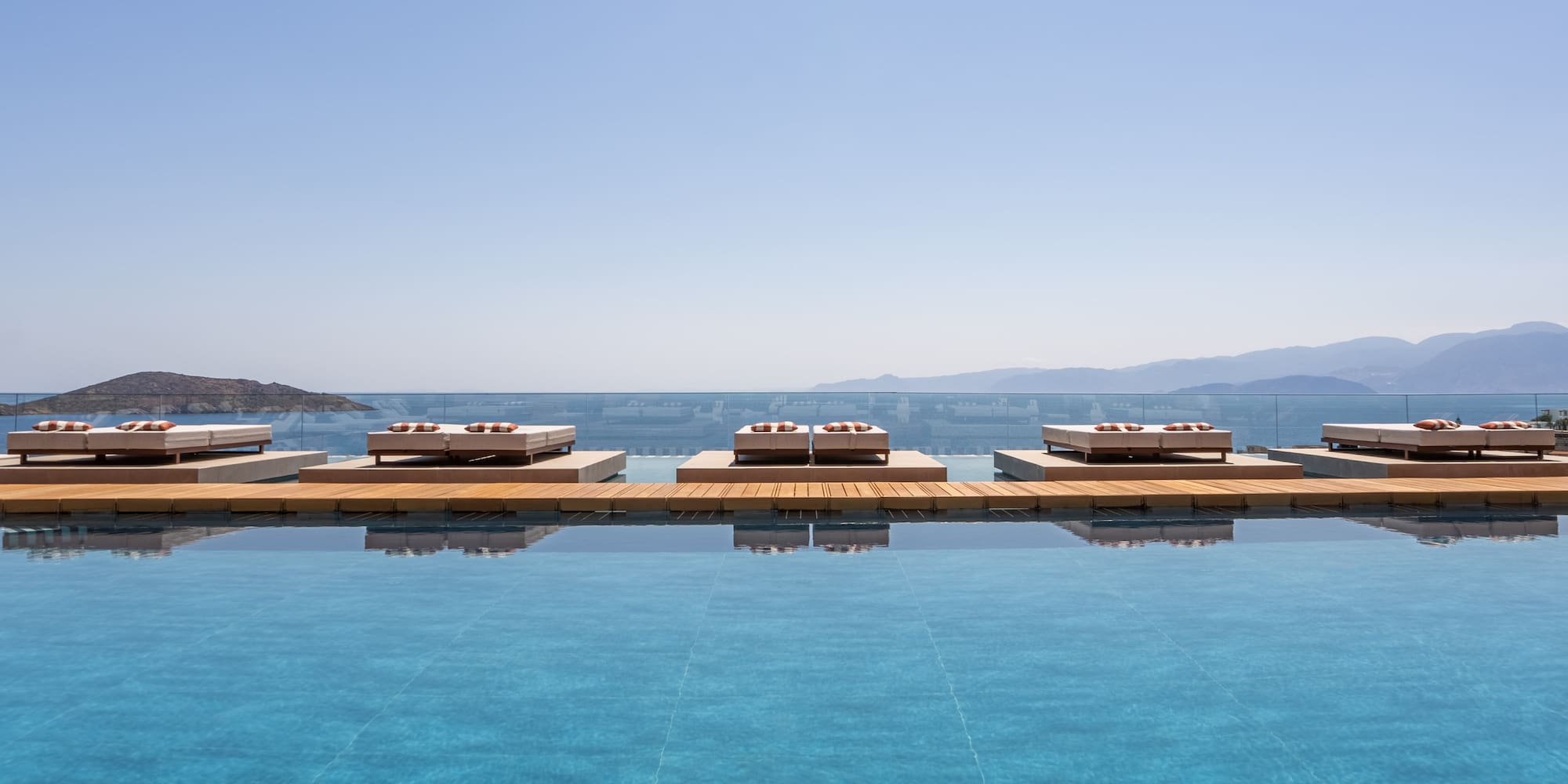 Luxury resort infinity pool with daybeds, ocean, and mountain view.
