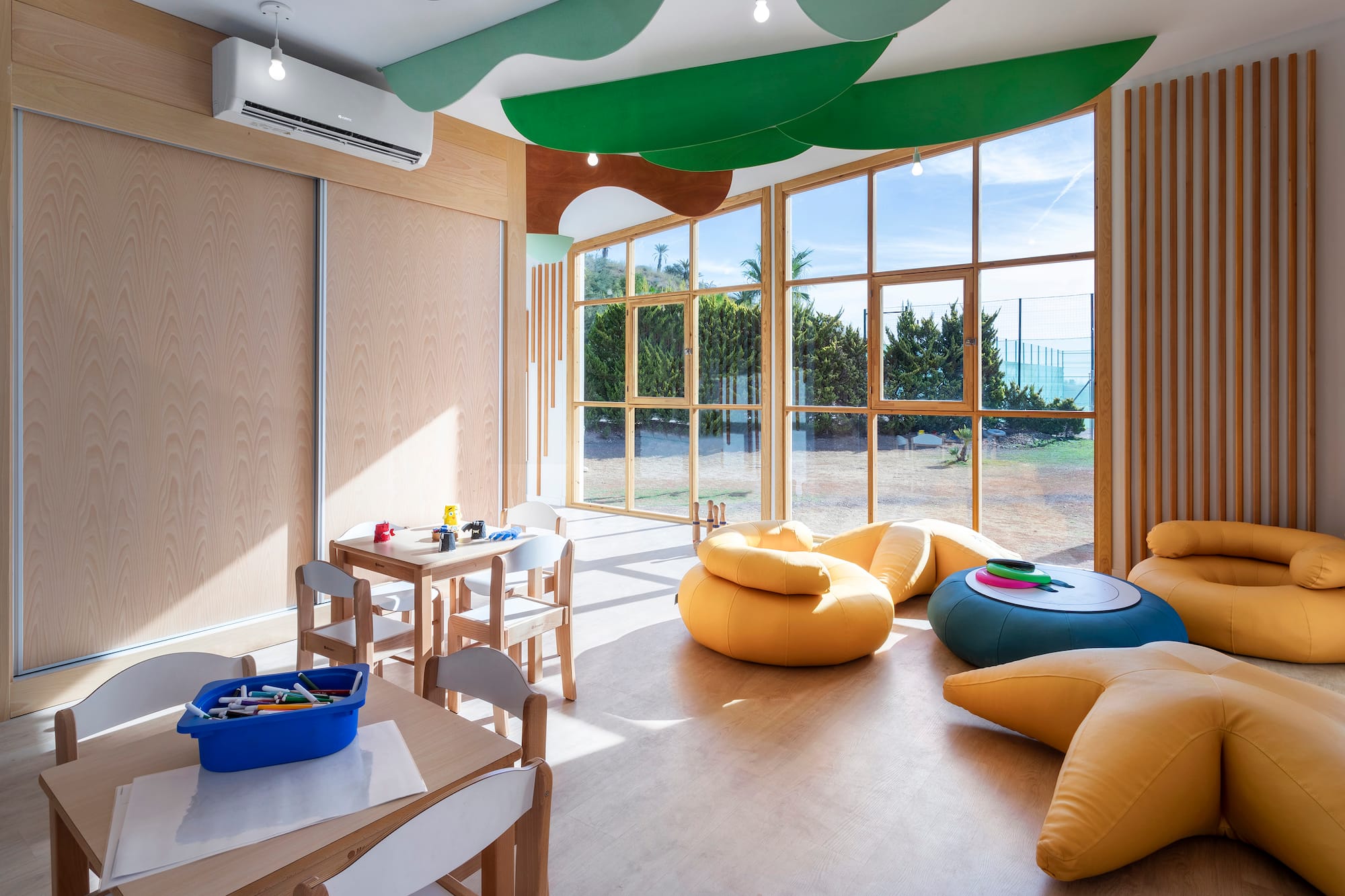 Modern kids' play area with wooden tables, colorful seating, and large windows.