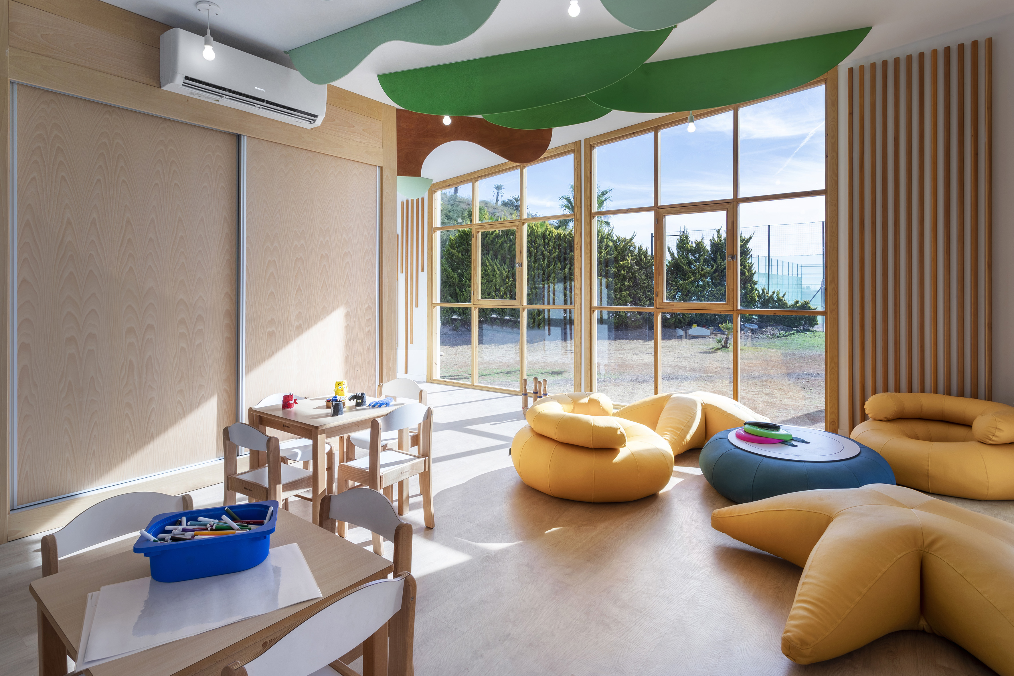 Modern kids' play area with wooden tables, colorful seating, and large windows.