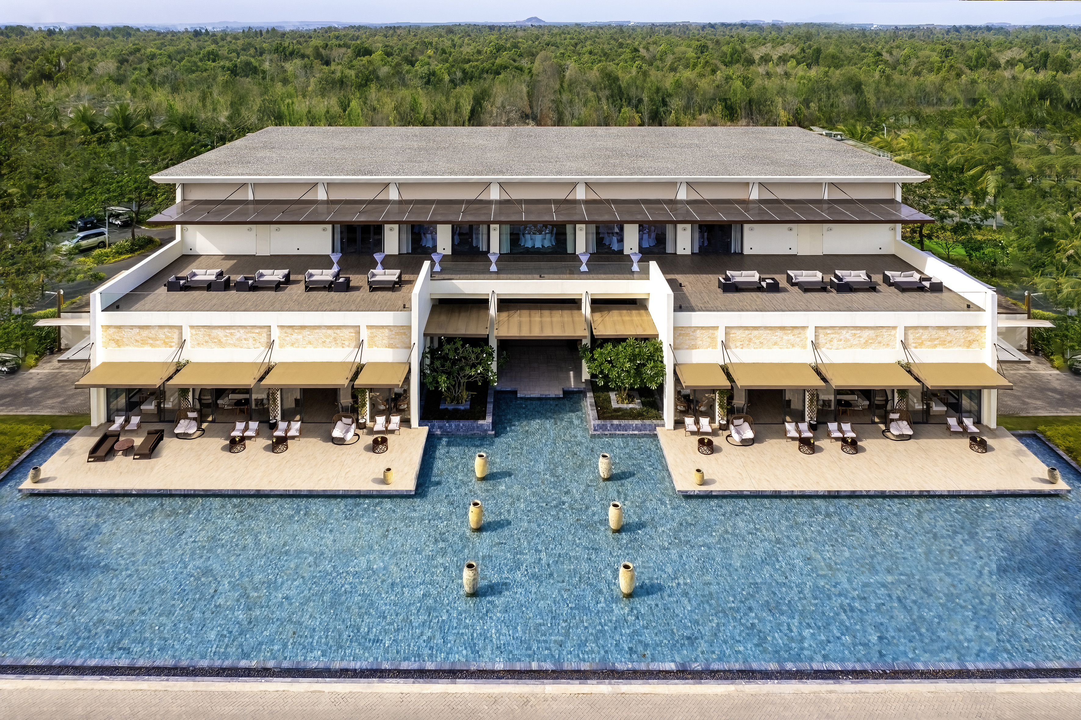 Modern resort hotel with swimming pool, outdoor terraces, and green forest.