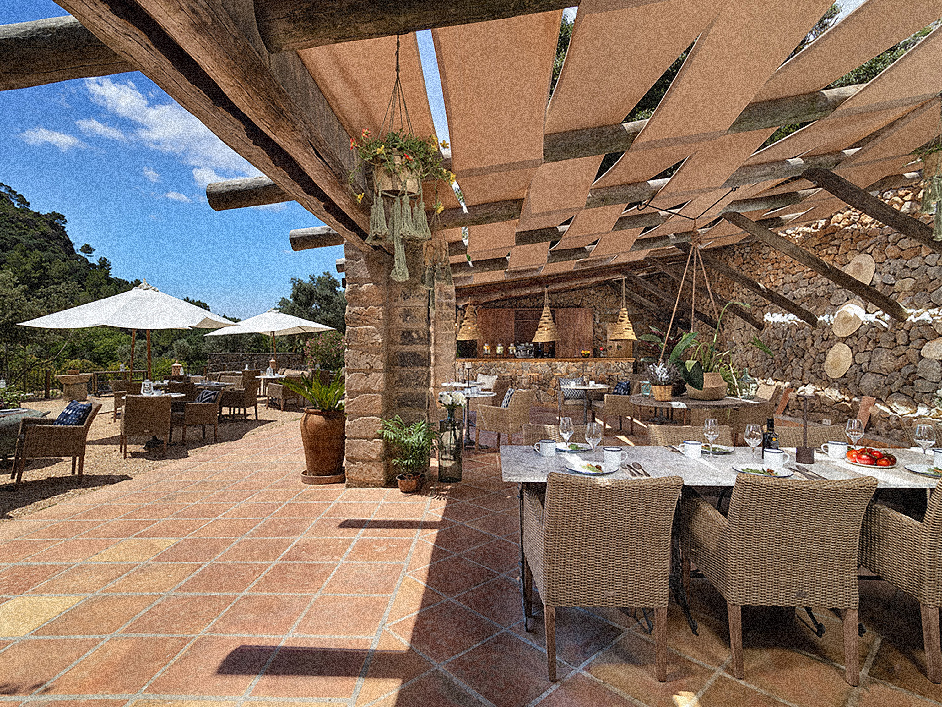 Outdoor restaurant patio with terracotta floor, shaded pergola, and wicker dining.