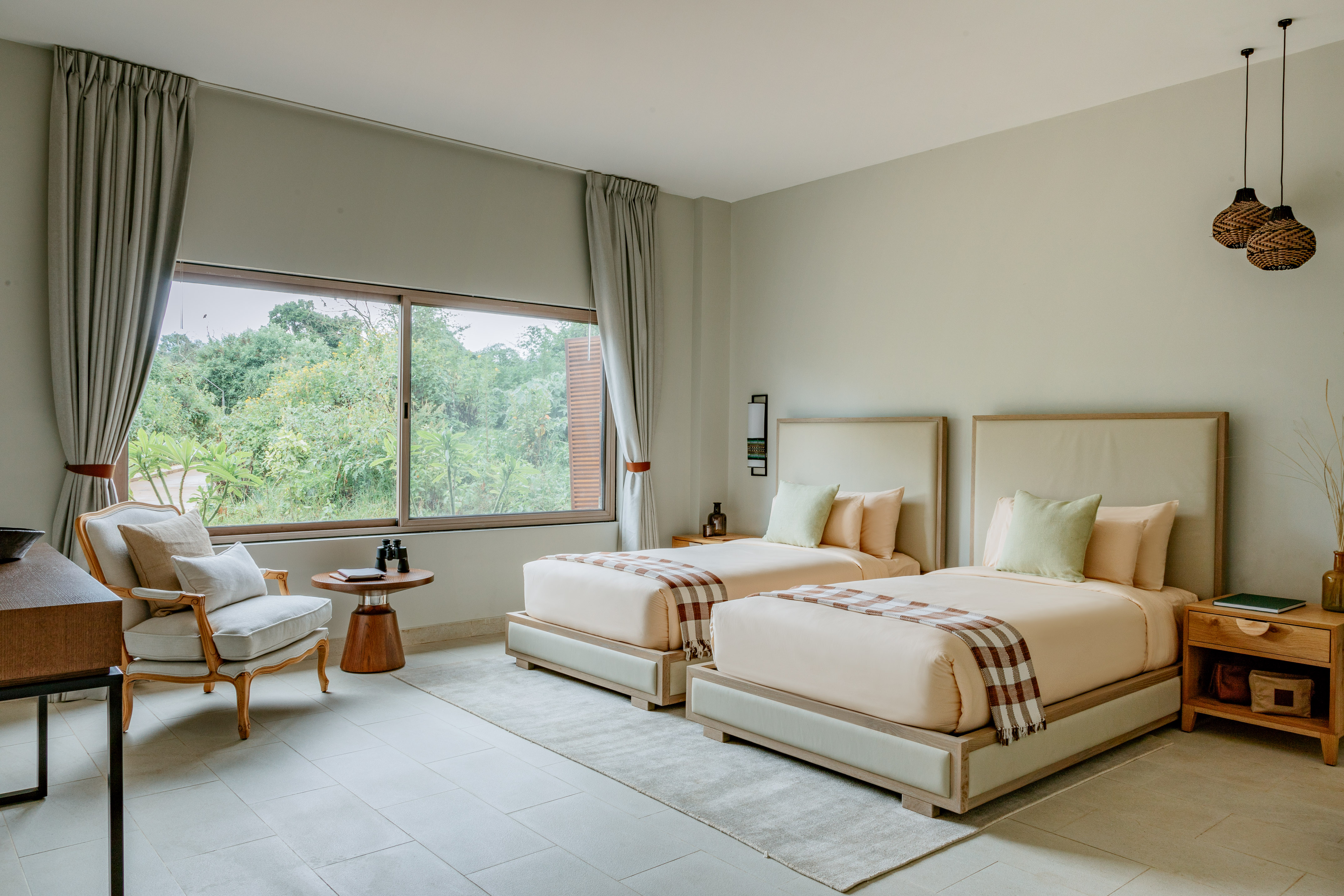 Modern hotel room with two twin beds, large window, and green forest view.