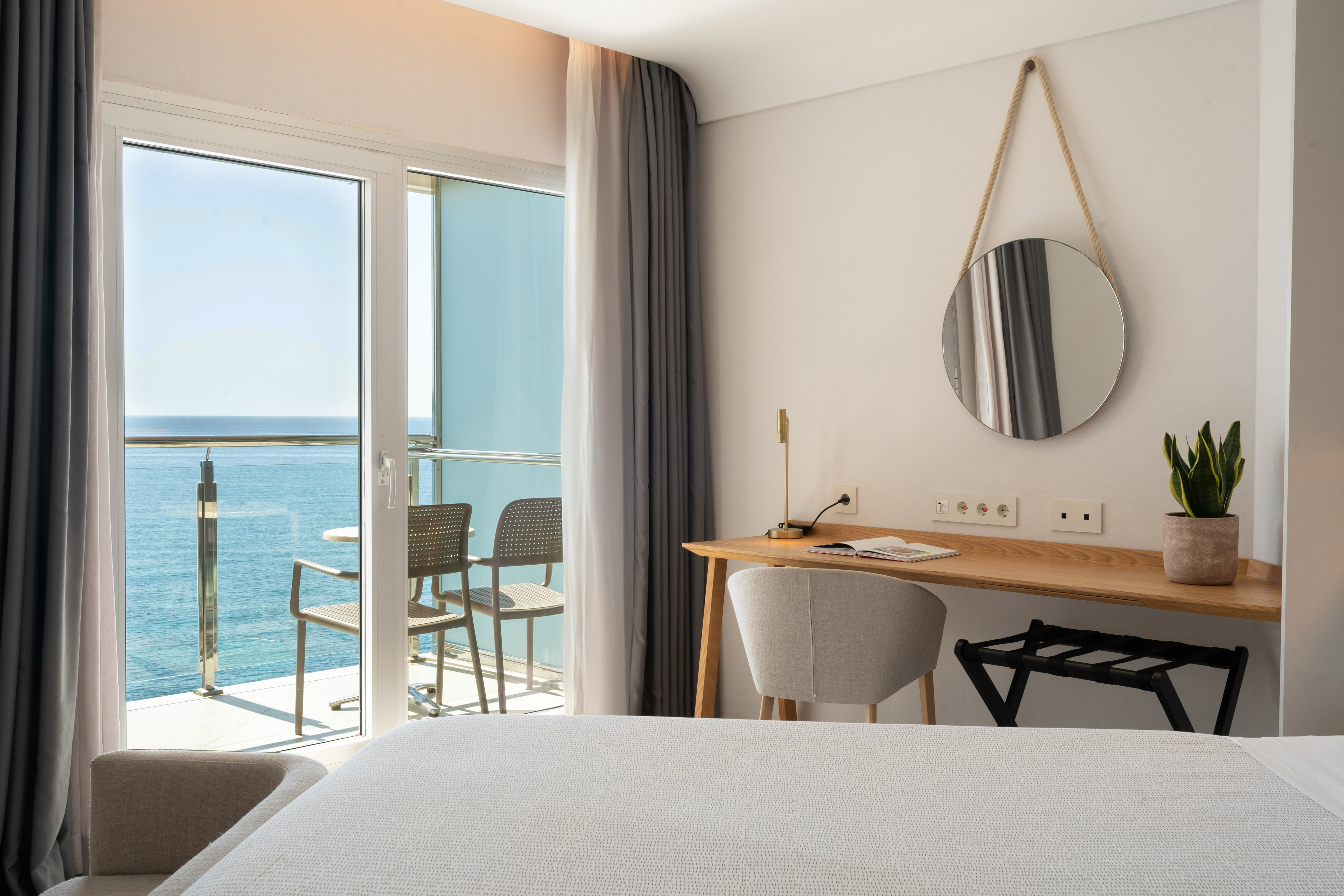 Modern hotel room with sea view balcony, desk, and round mirror.